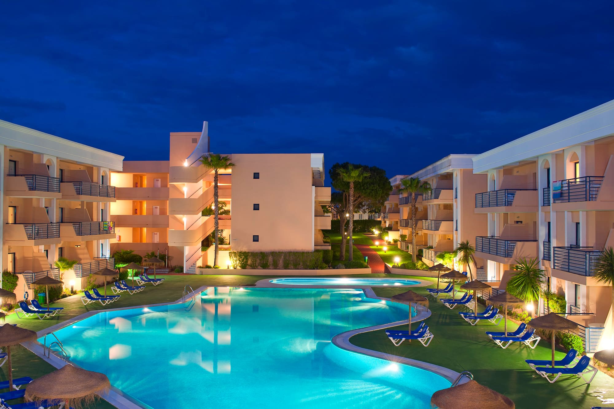 a pool with lounge chairs and a building with a dark sky