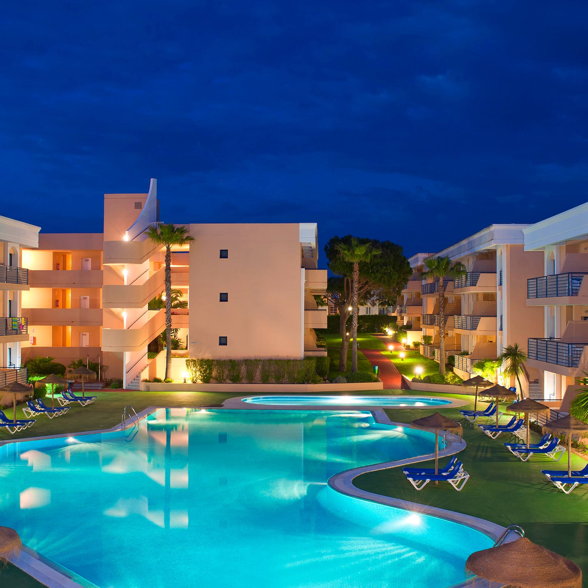 a pool with lounge chairs and a building with a dark sky