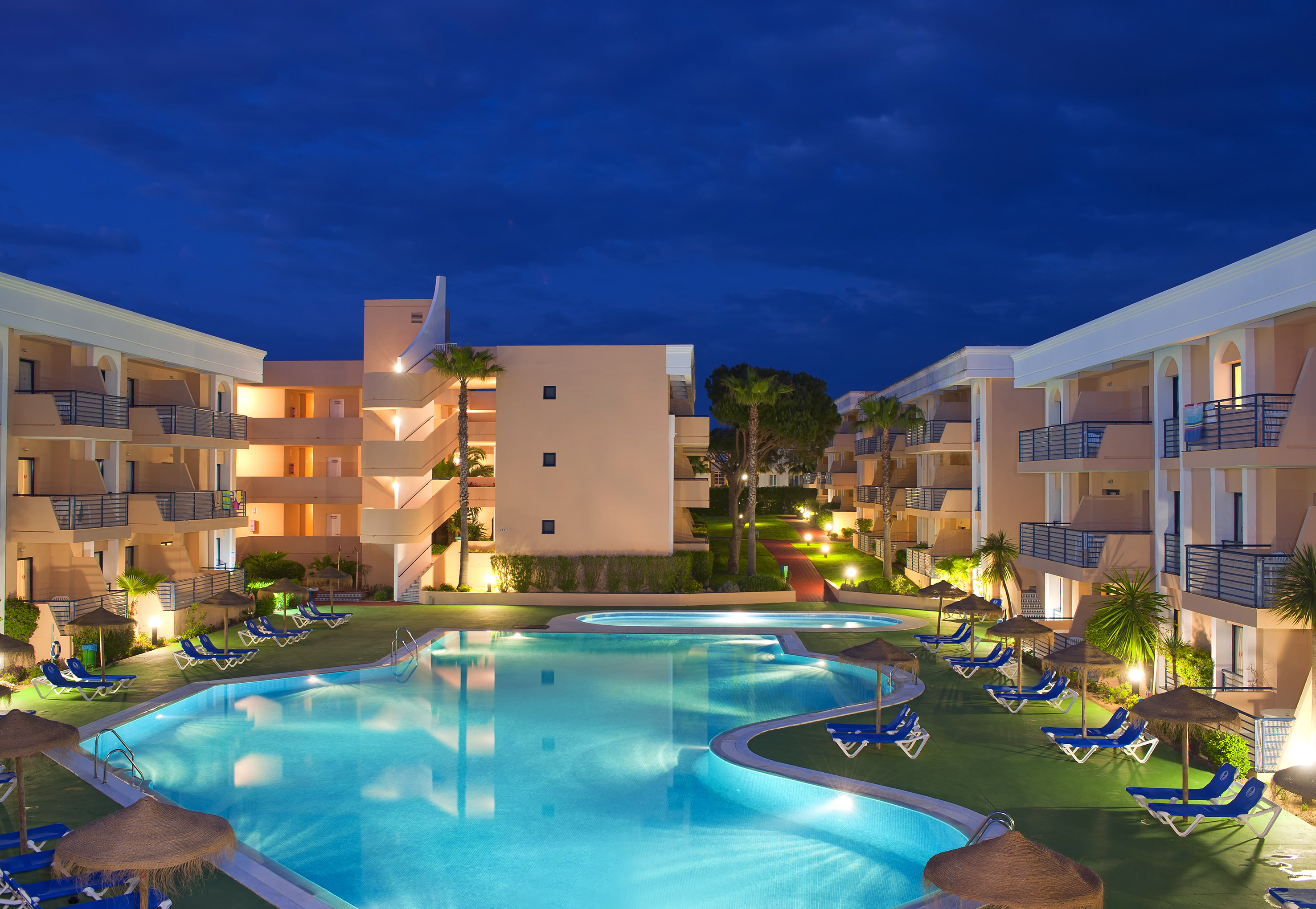 a pool with lounge chairs and a building with a dark sky
