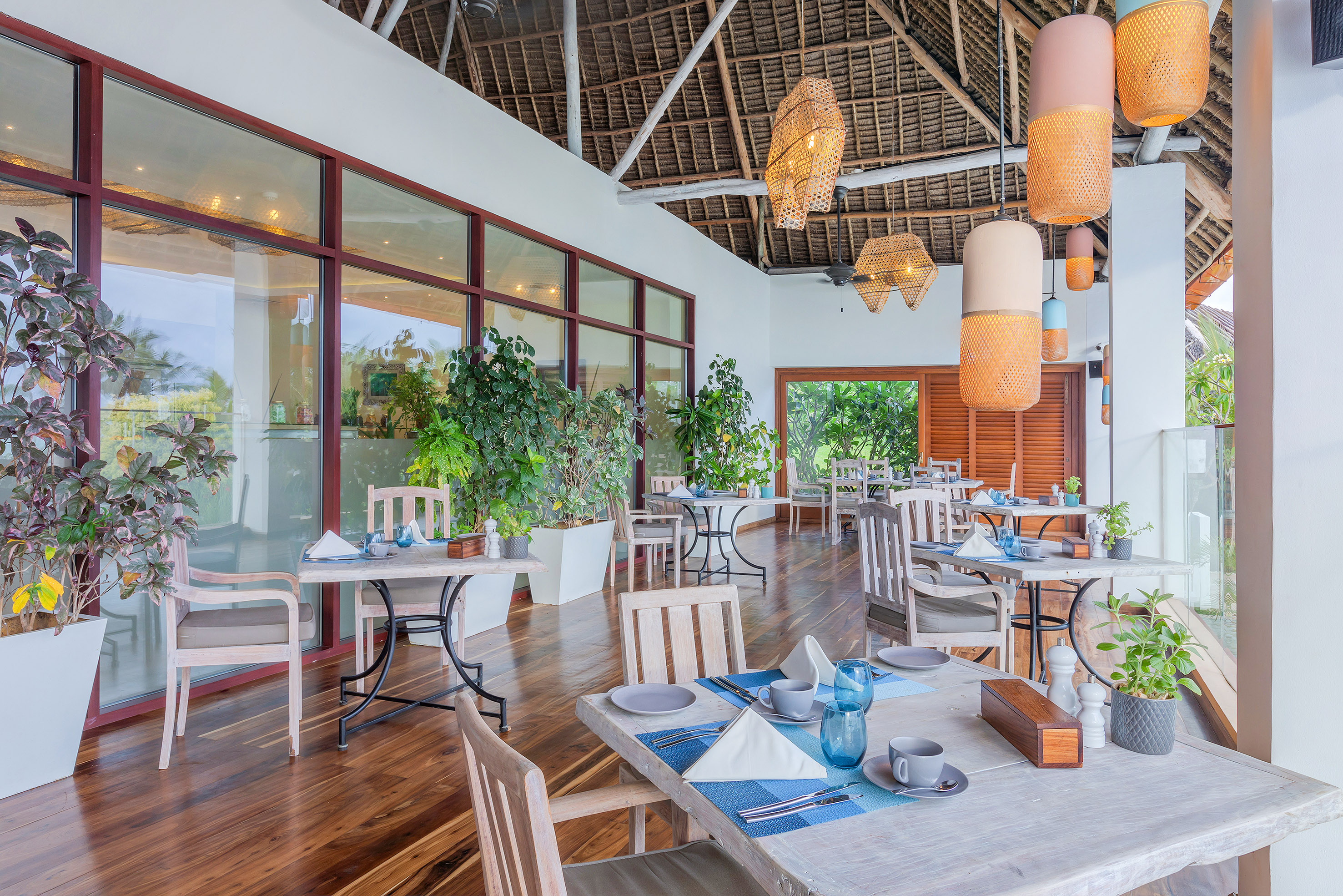 Tropical resort dining with thatch roof, wooden tables, and woven lights.