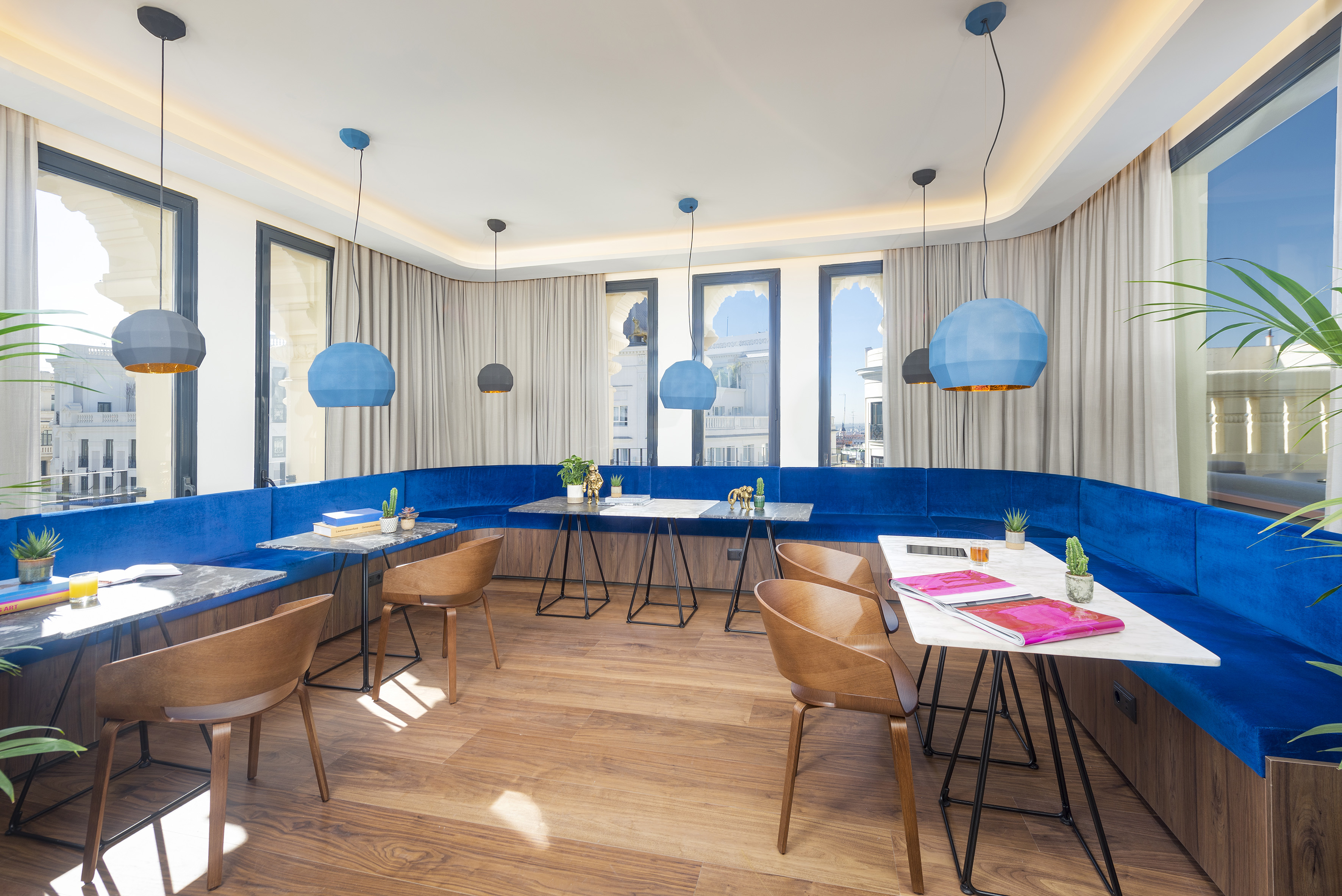 Modern cafe lounge with blue velvet banquette, marble tables, and pendant lights.