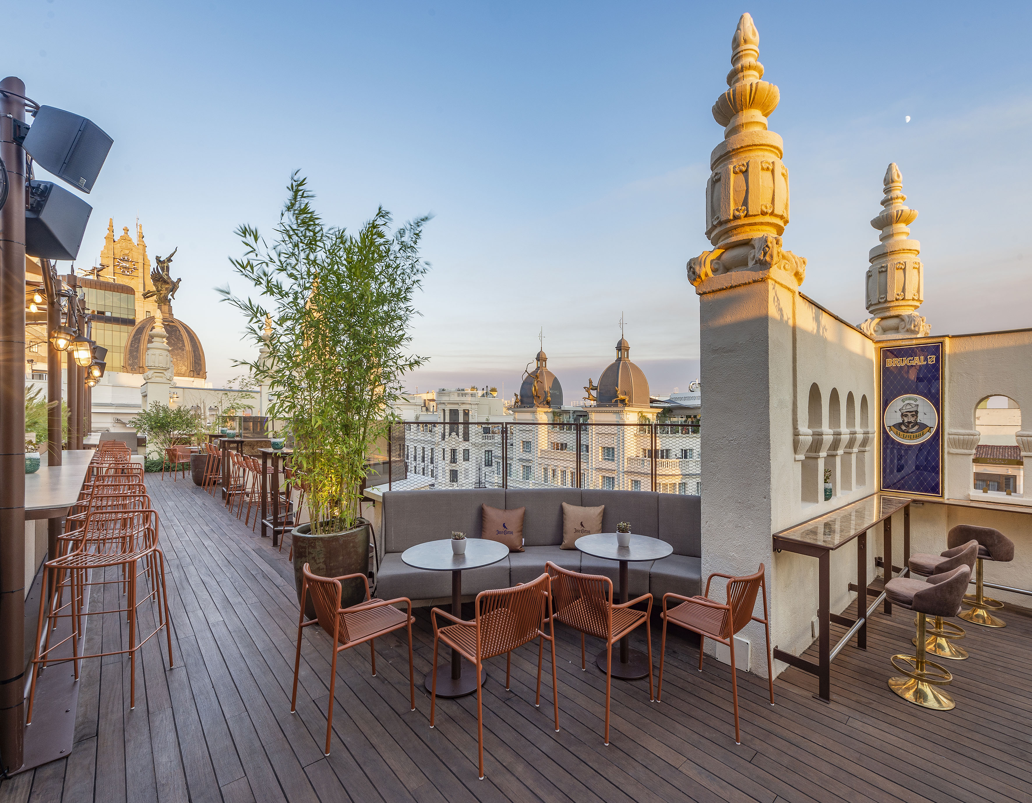 Rooftop bar with modern seating, city skyline, and historical domes.