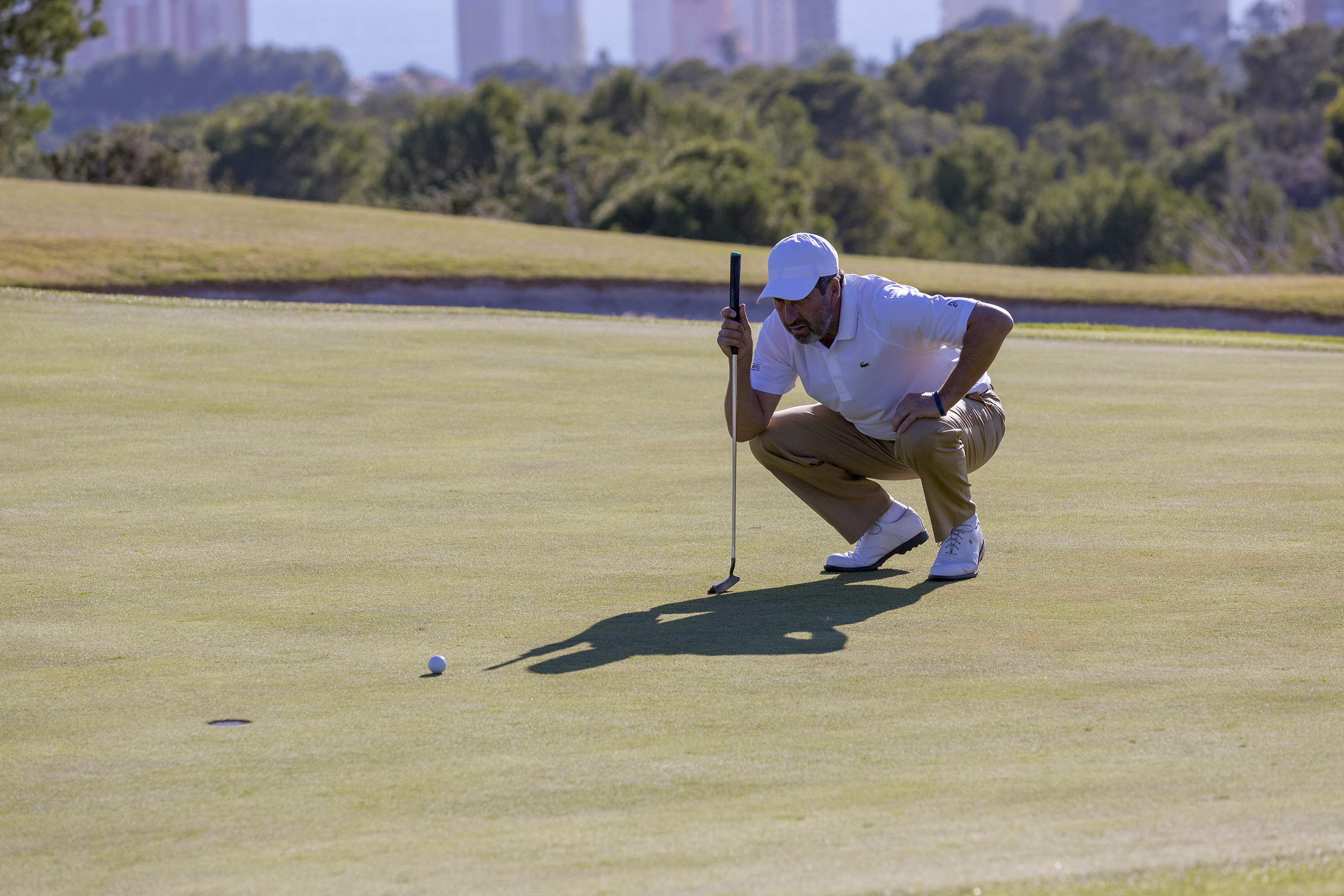 Golfer reading a putt on the green, with golf ball and putter.