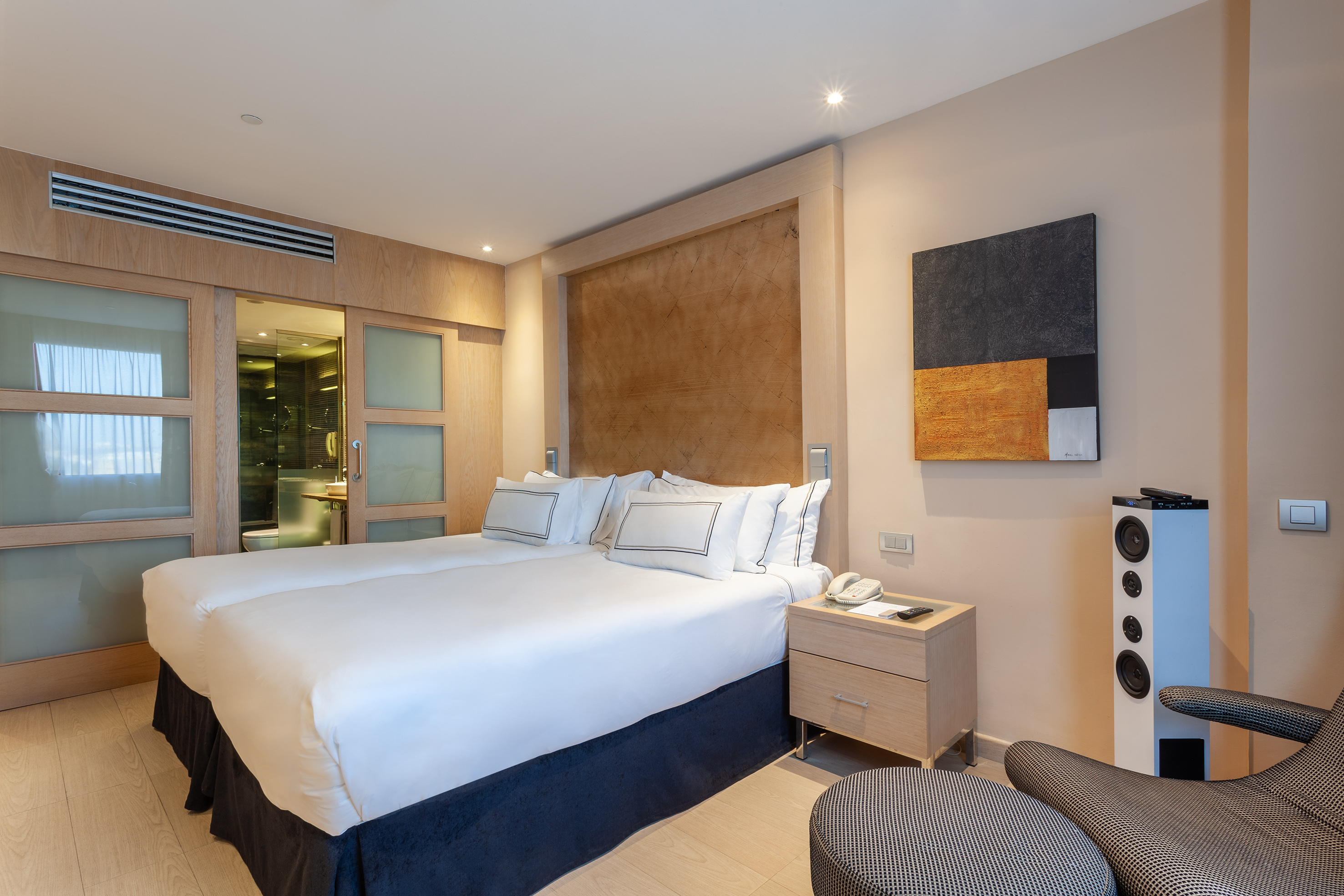 Modern hotel bedroom with two beds, wooden headboard, abstract art, and ensuite bathroom.