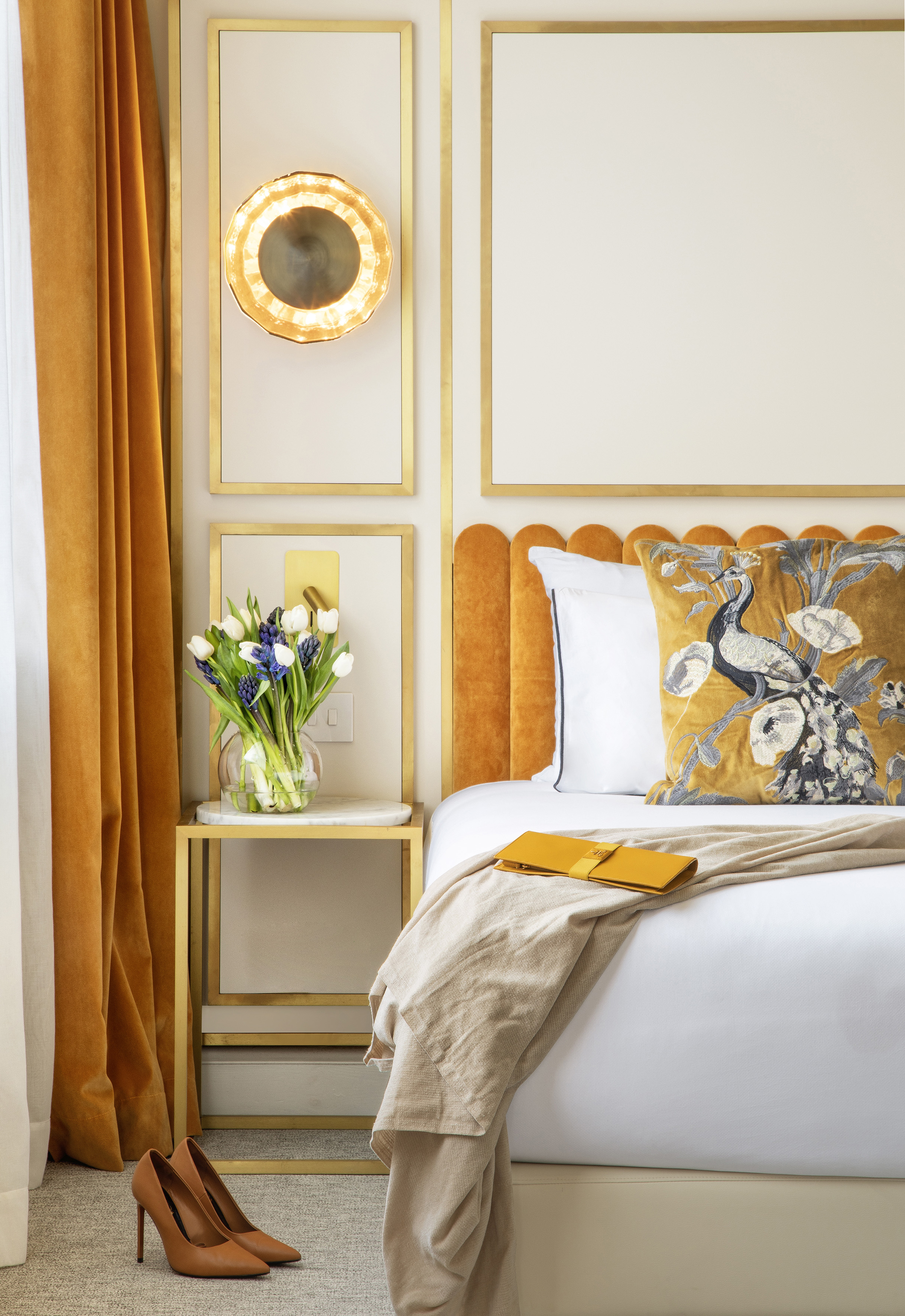 Luxury bedroom with gold scalloped headboard, peacock pillow, and floral accents.