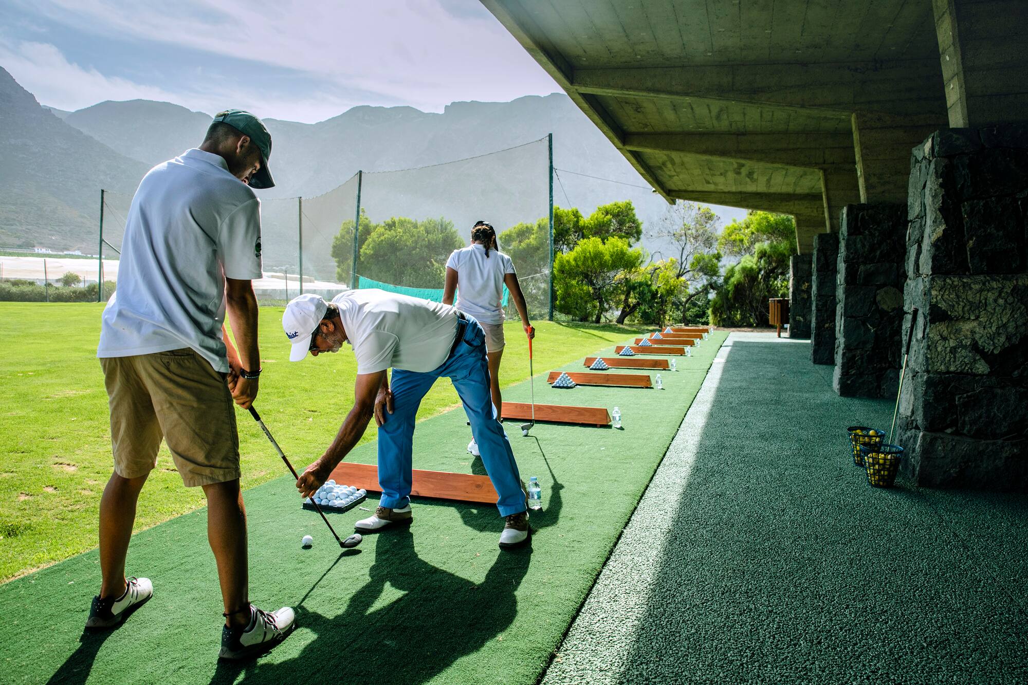 Golfers practicing swings at a scenic outdoor driving range.