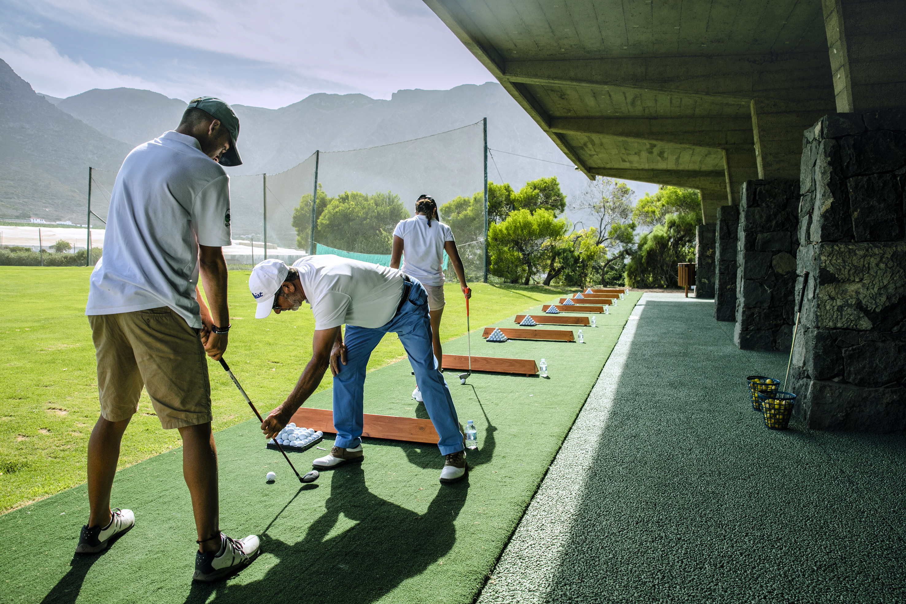 Golfers practicing swings at a scenic outdoor driving range.
