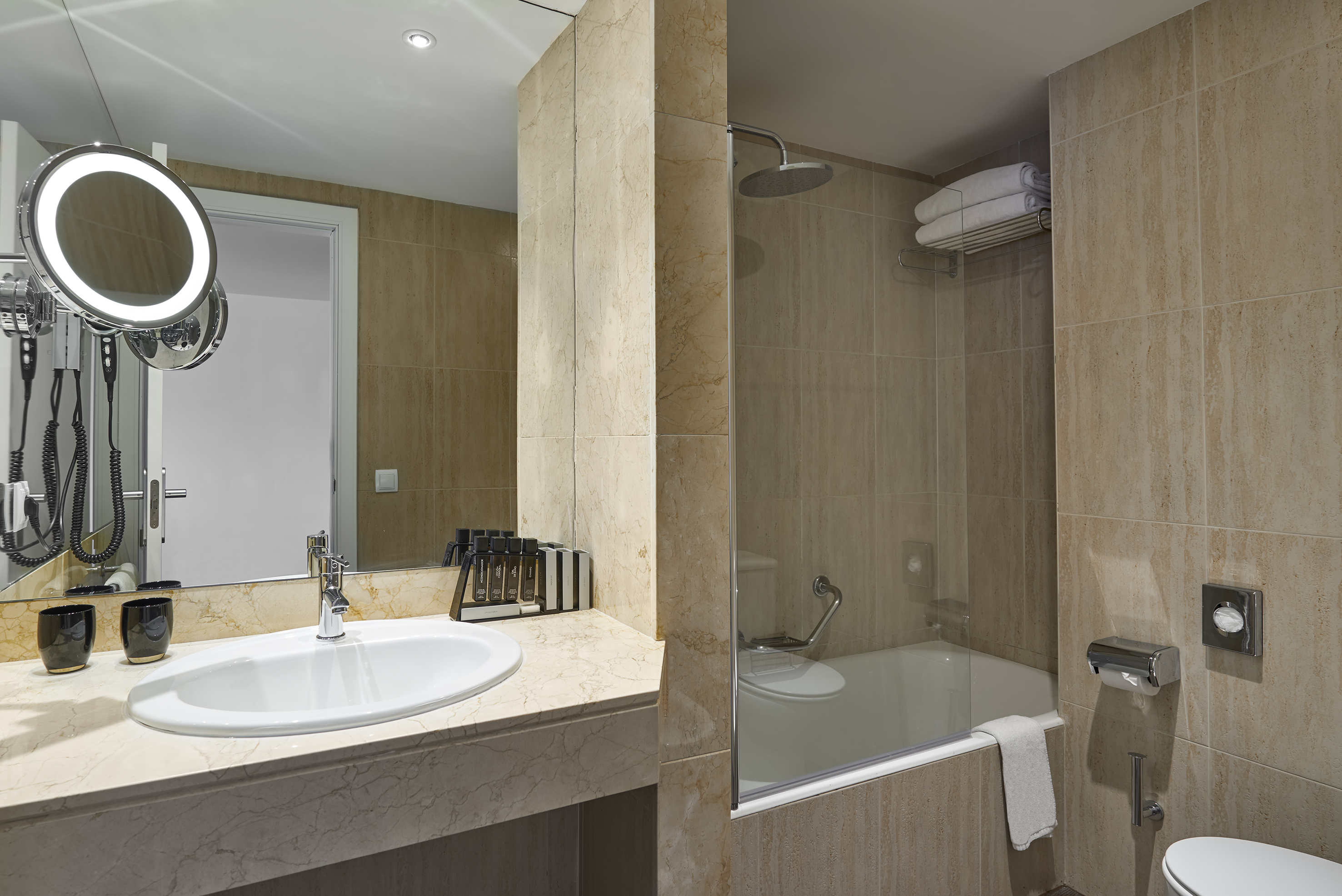 Modern beige tiled bathroom with vanity, lighted mirror, shower, and tub.