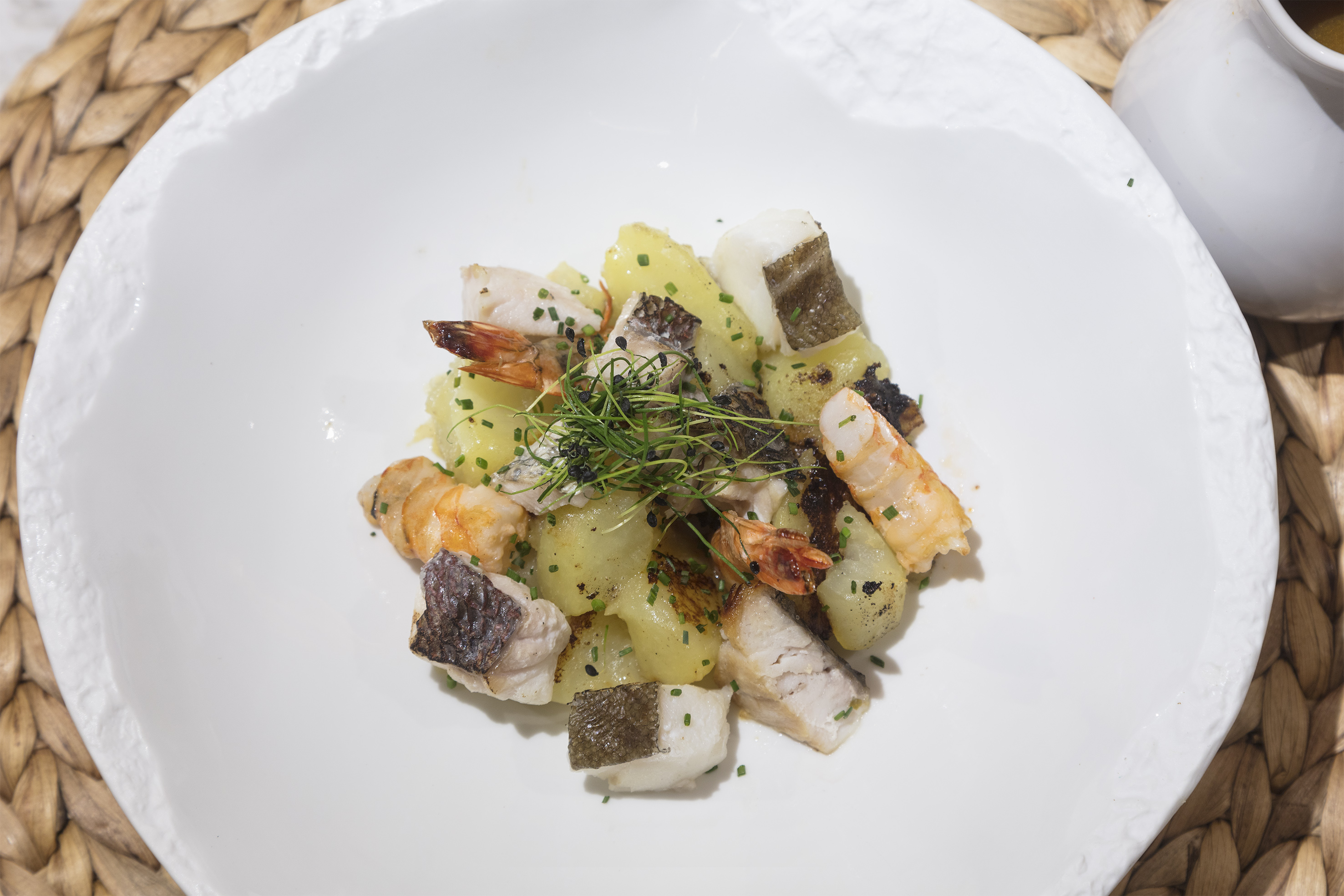 Gourmet seafood dish with fish, shrimp, and potatoes, garnished with chives on white plate.