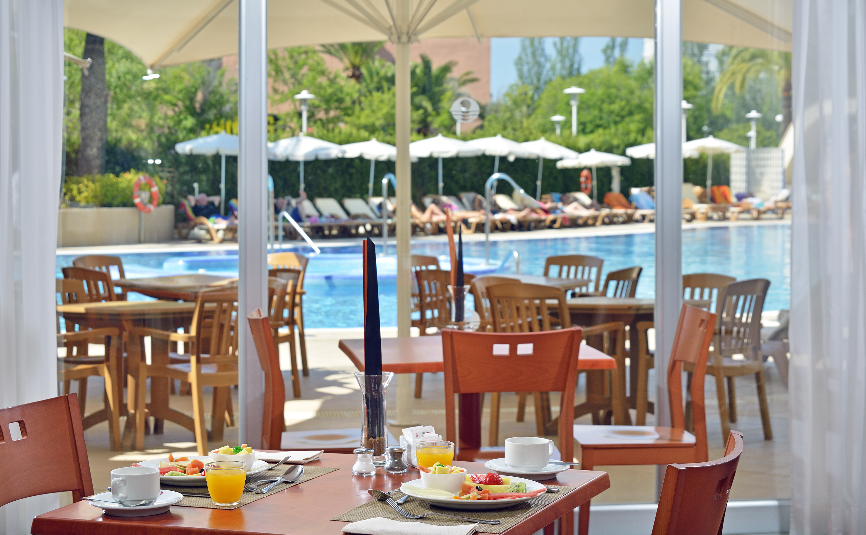Breakfast with fruit & juice at hotel restaurant, sunny resort pool view.