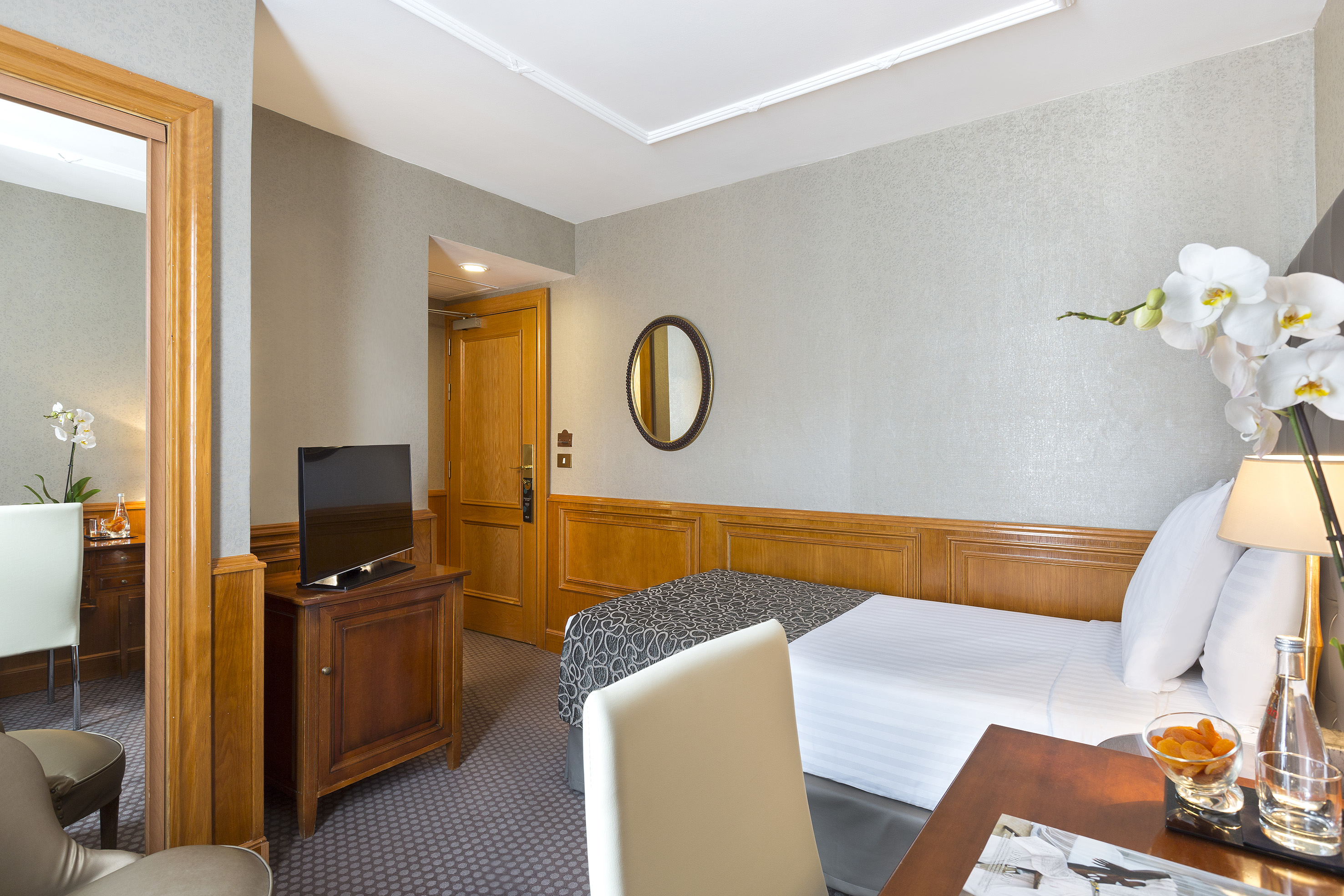 Hotel guest room with single bed, TV, wood furniture, and orchids.