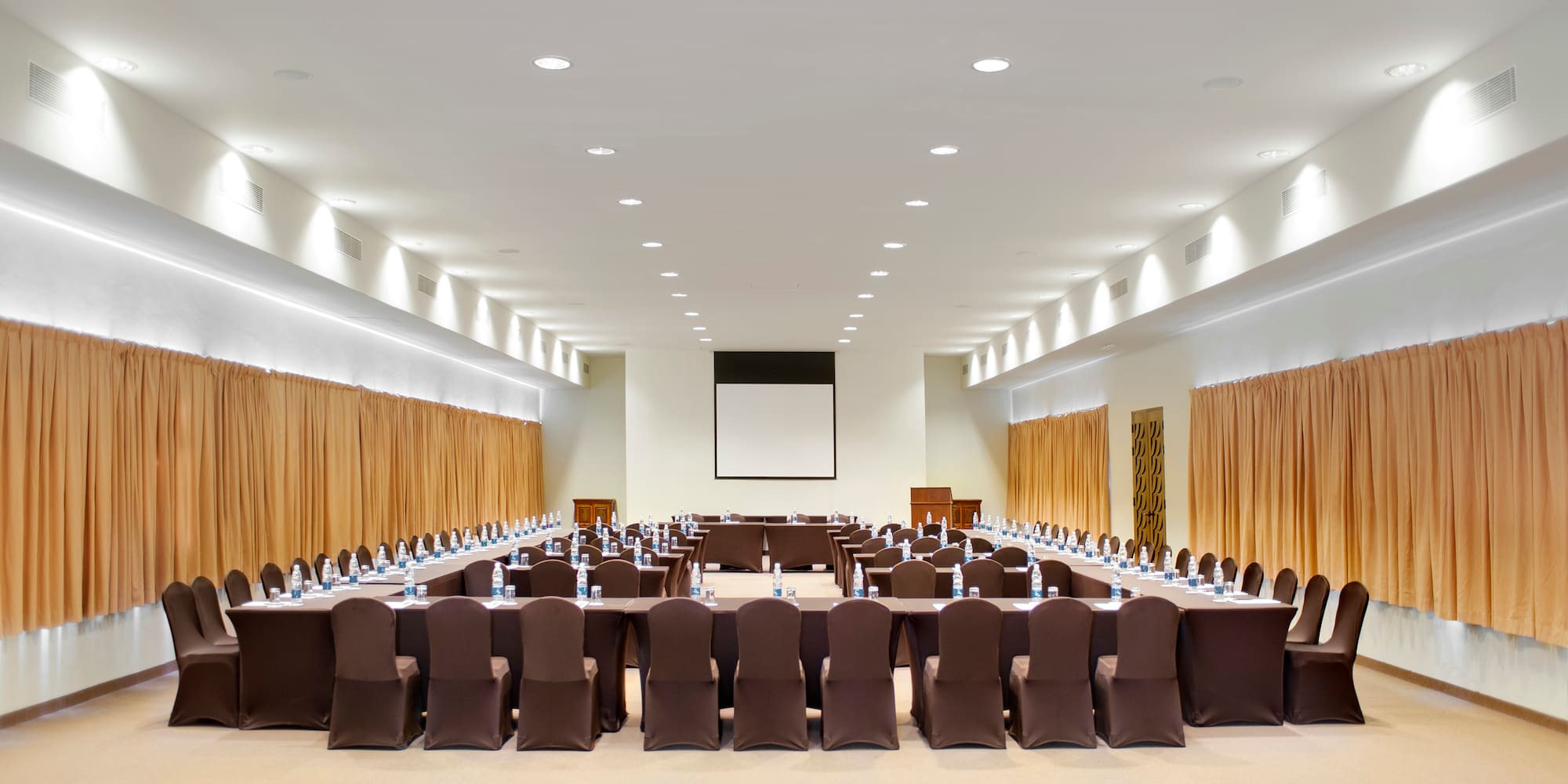 a large conference room with brown chairs and a projector screen