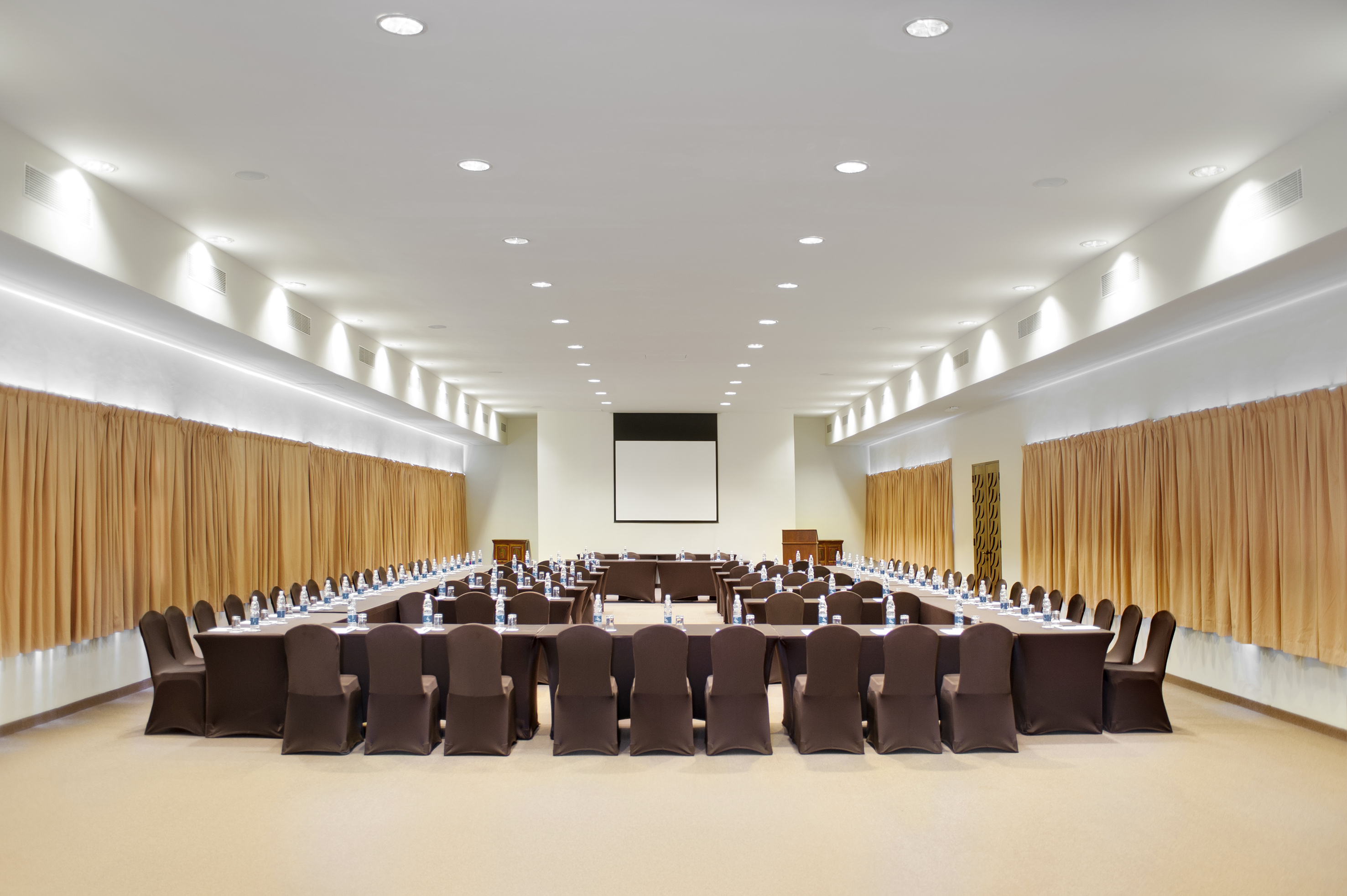 U-shape meeting room with presentation screen and brown chairs for events.
