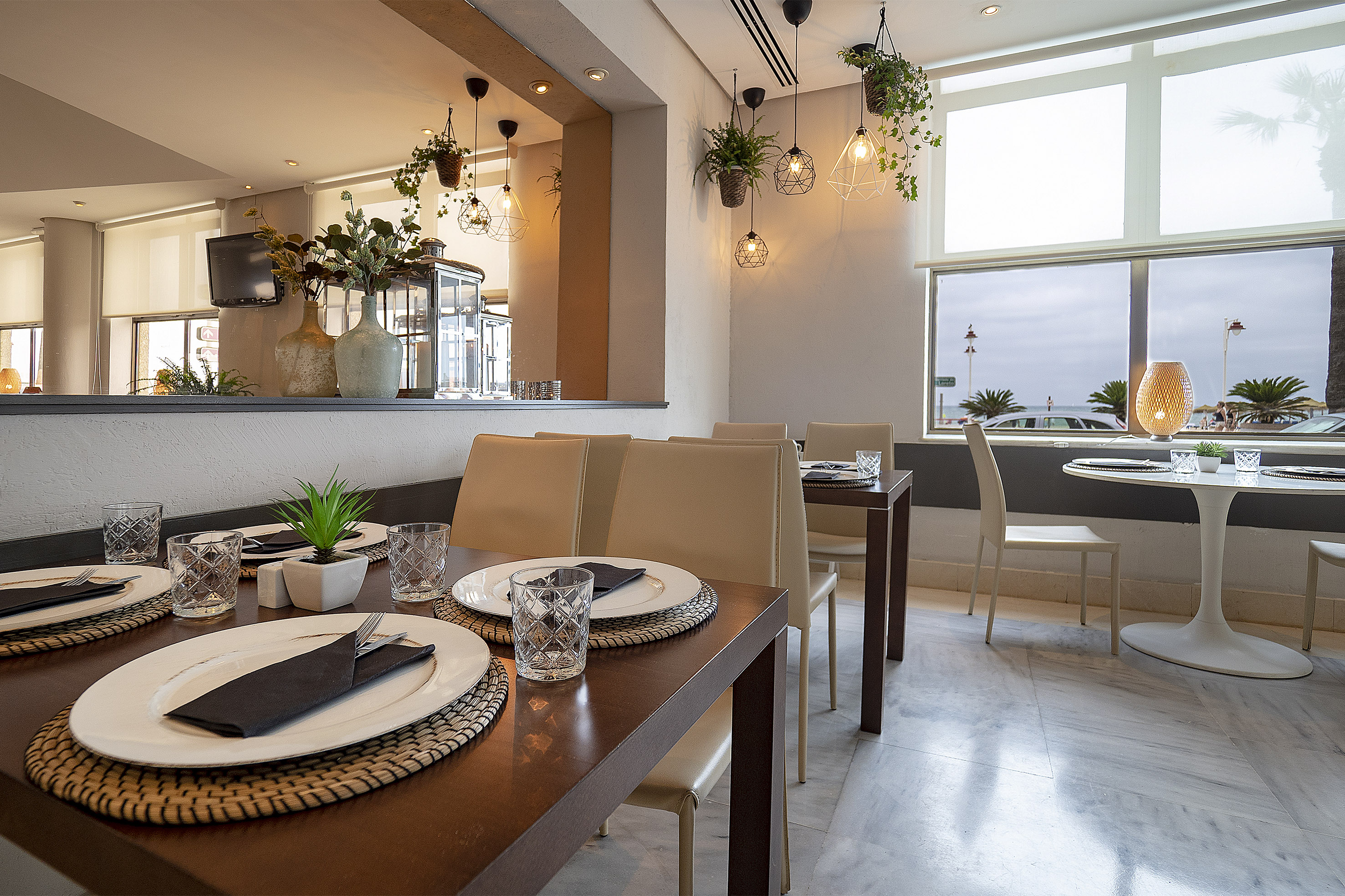 Coastal restaurant dining room with set tables, modern decor, and sea view windows.