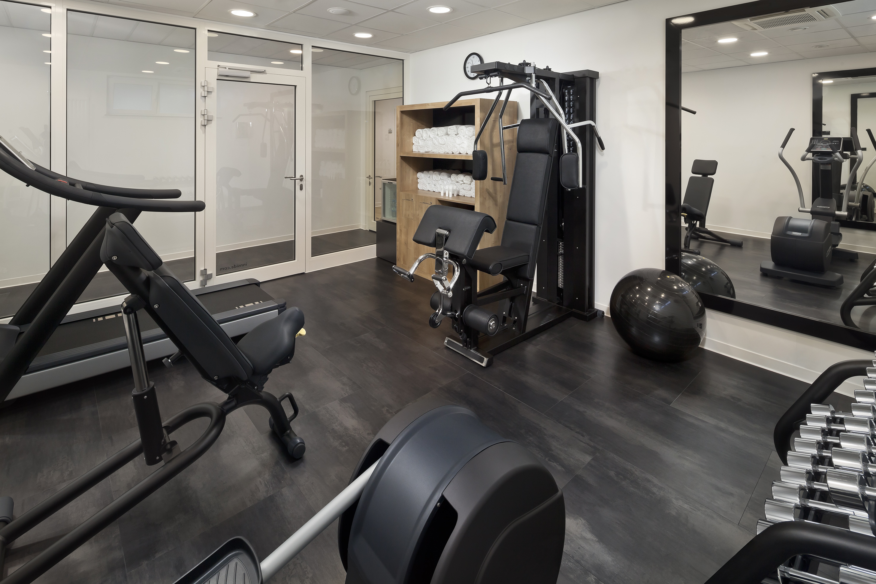 Modern hotel gym with cardio and strength training equipment, towels.