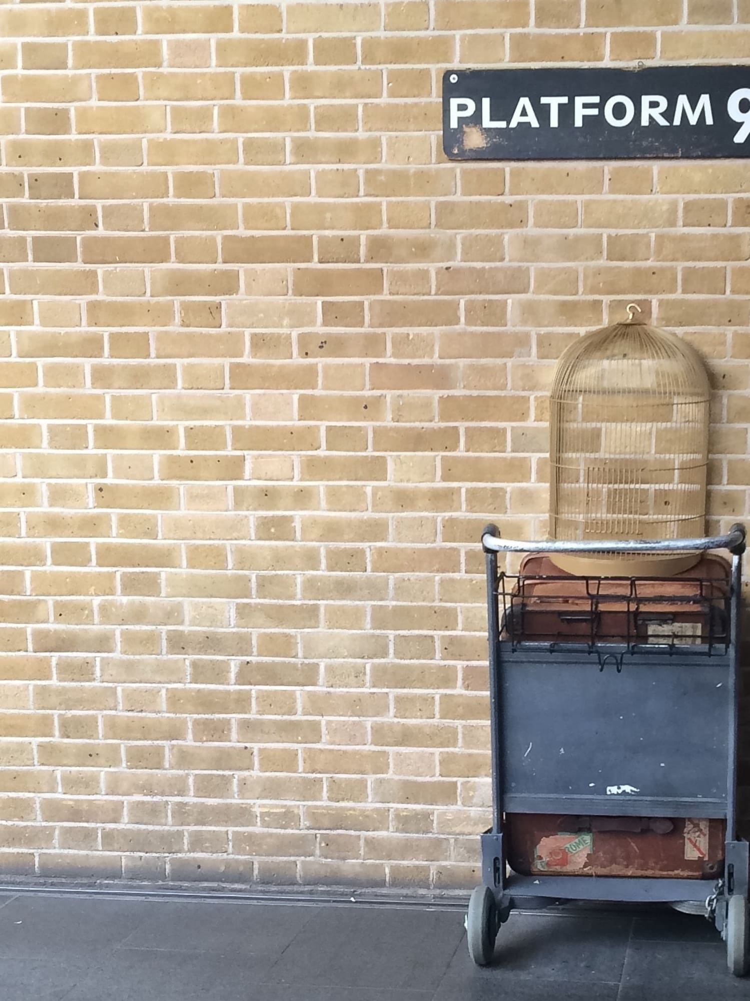 a cart with a bird cage on it leaning against a brick wall
