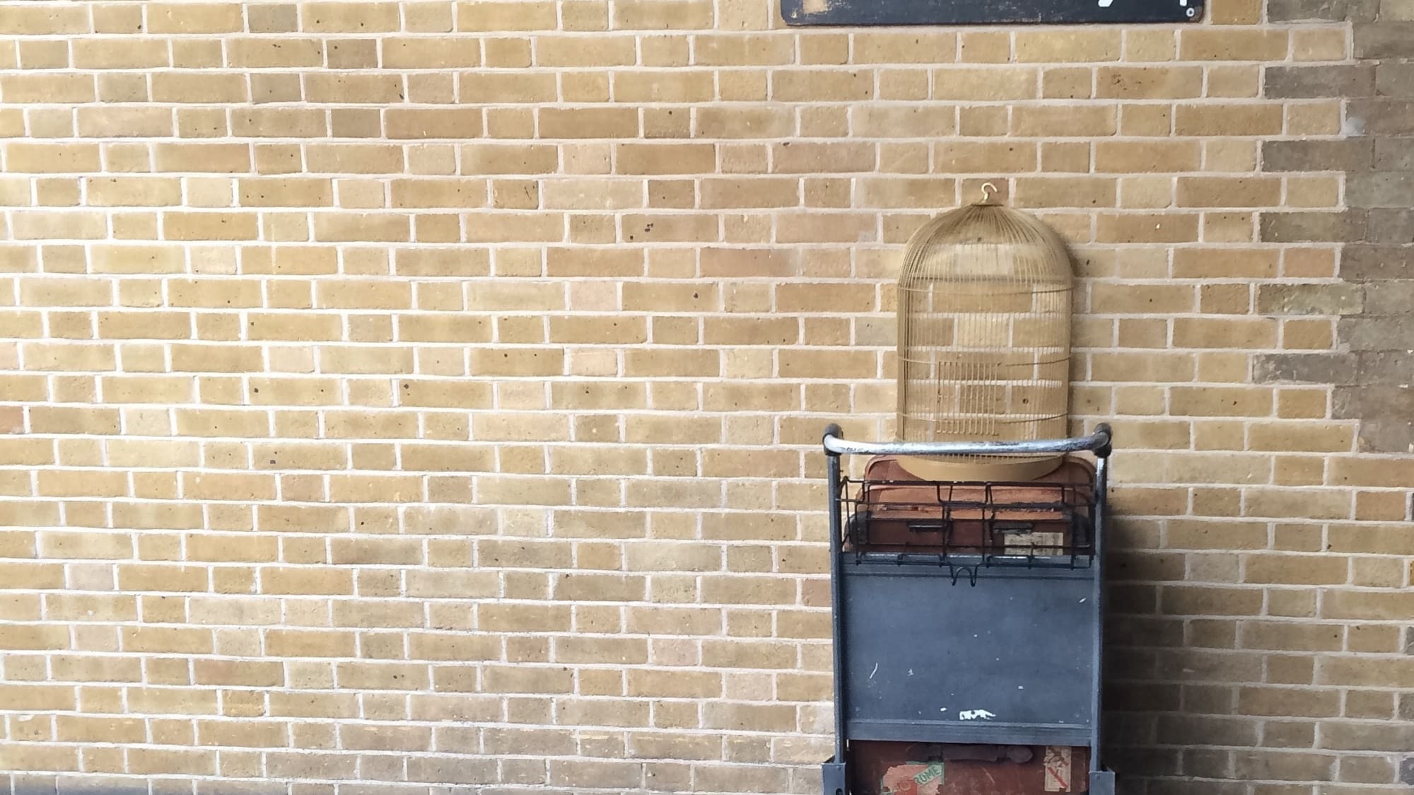 a cart with a bird cage on it leaning against a brick wall