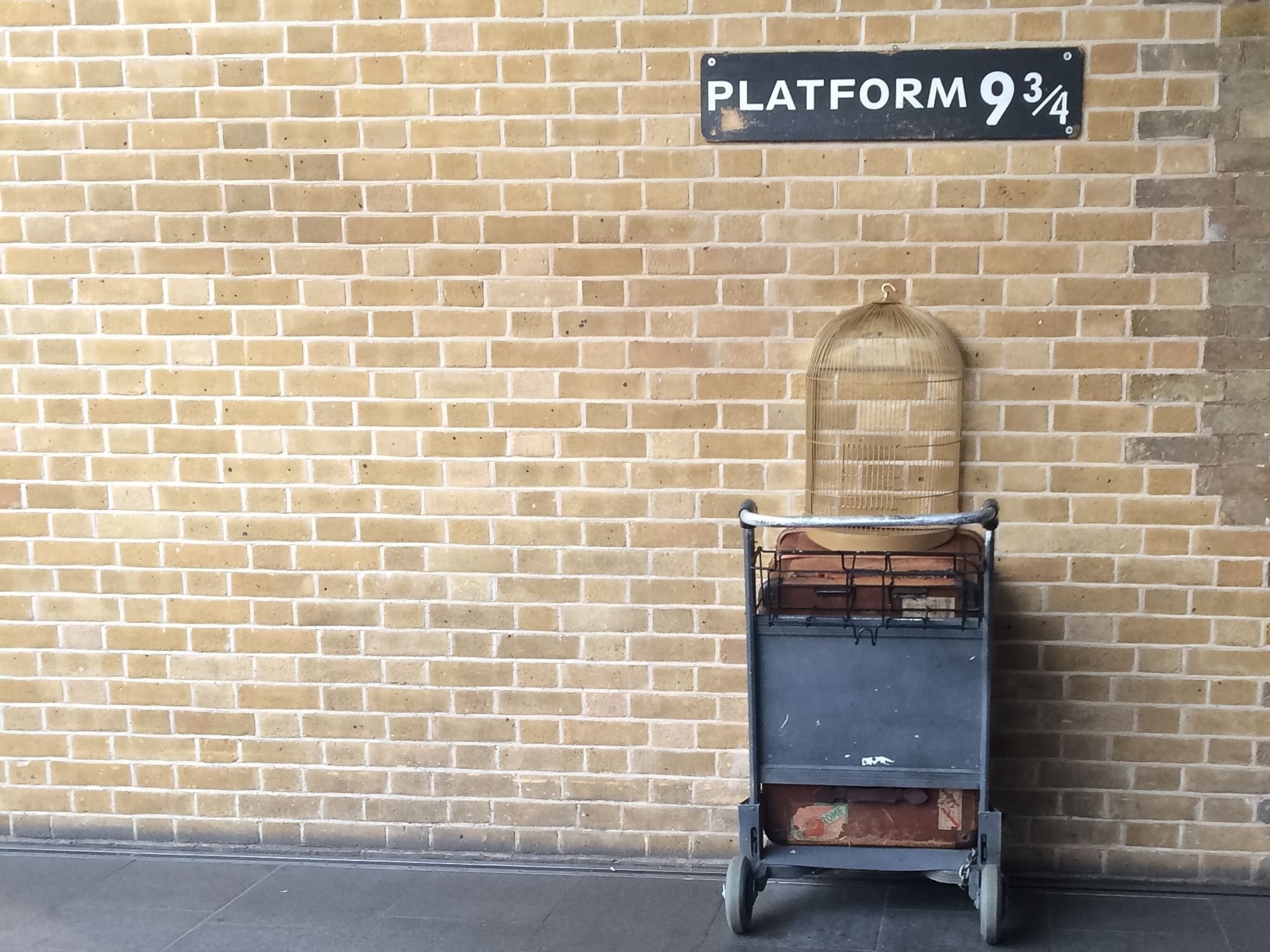 A cart rests against a brick wall, featuring a birdcage on top.