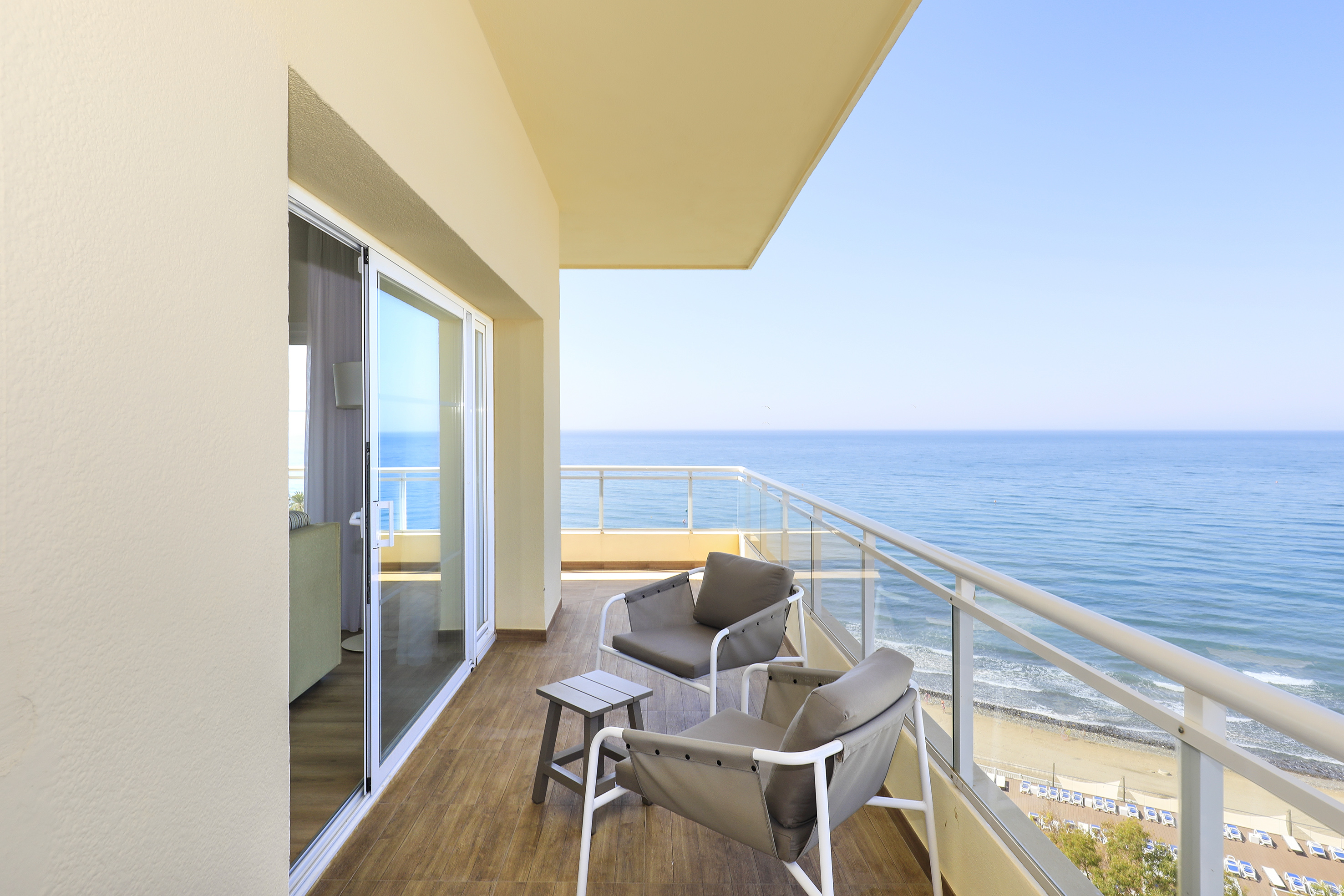 Ocean view balcony with two outdoor chairs, table, and beach.