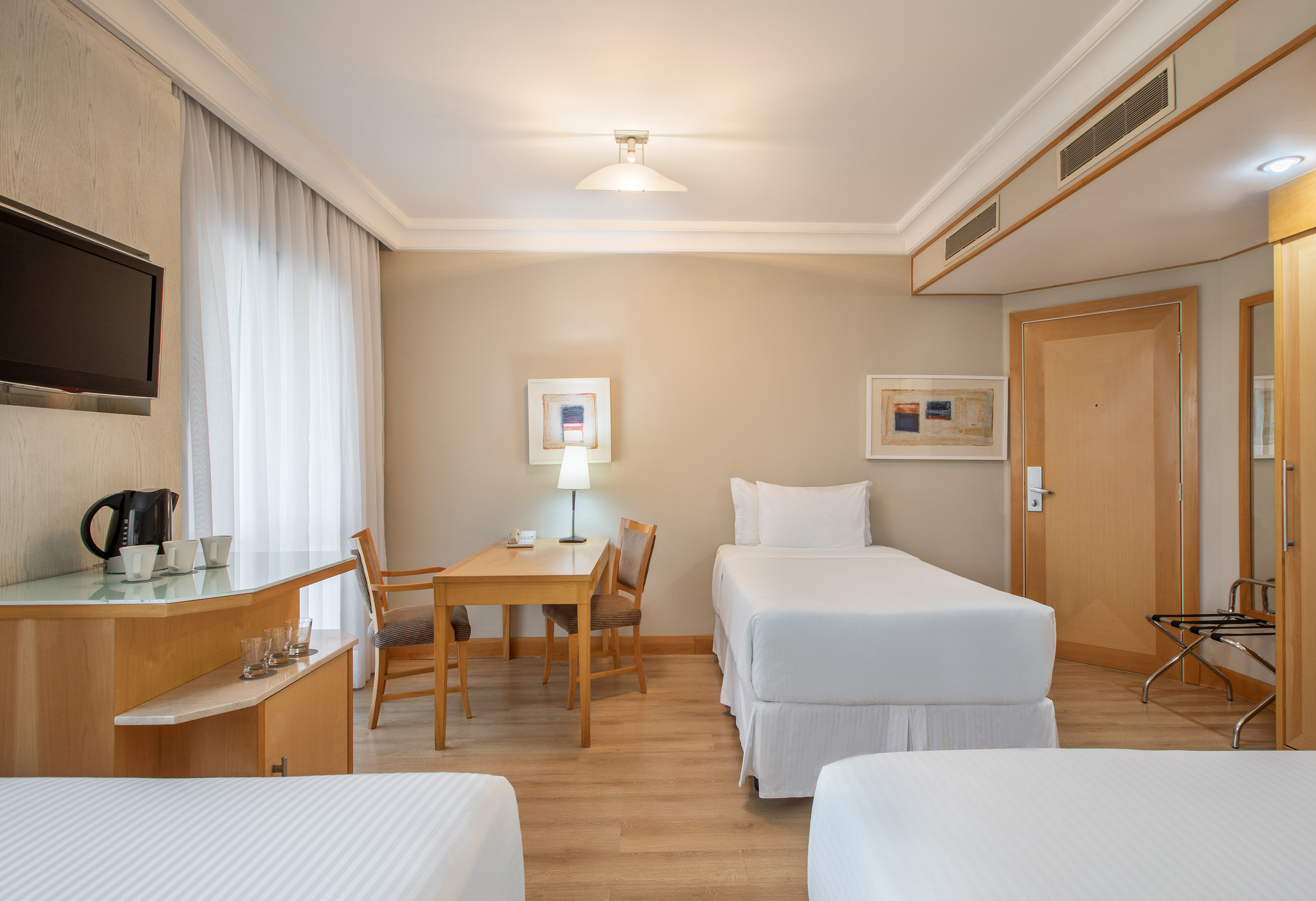 Hotel room with twin beds, wooden floor, work desk, TV, and coffee station.