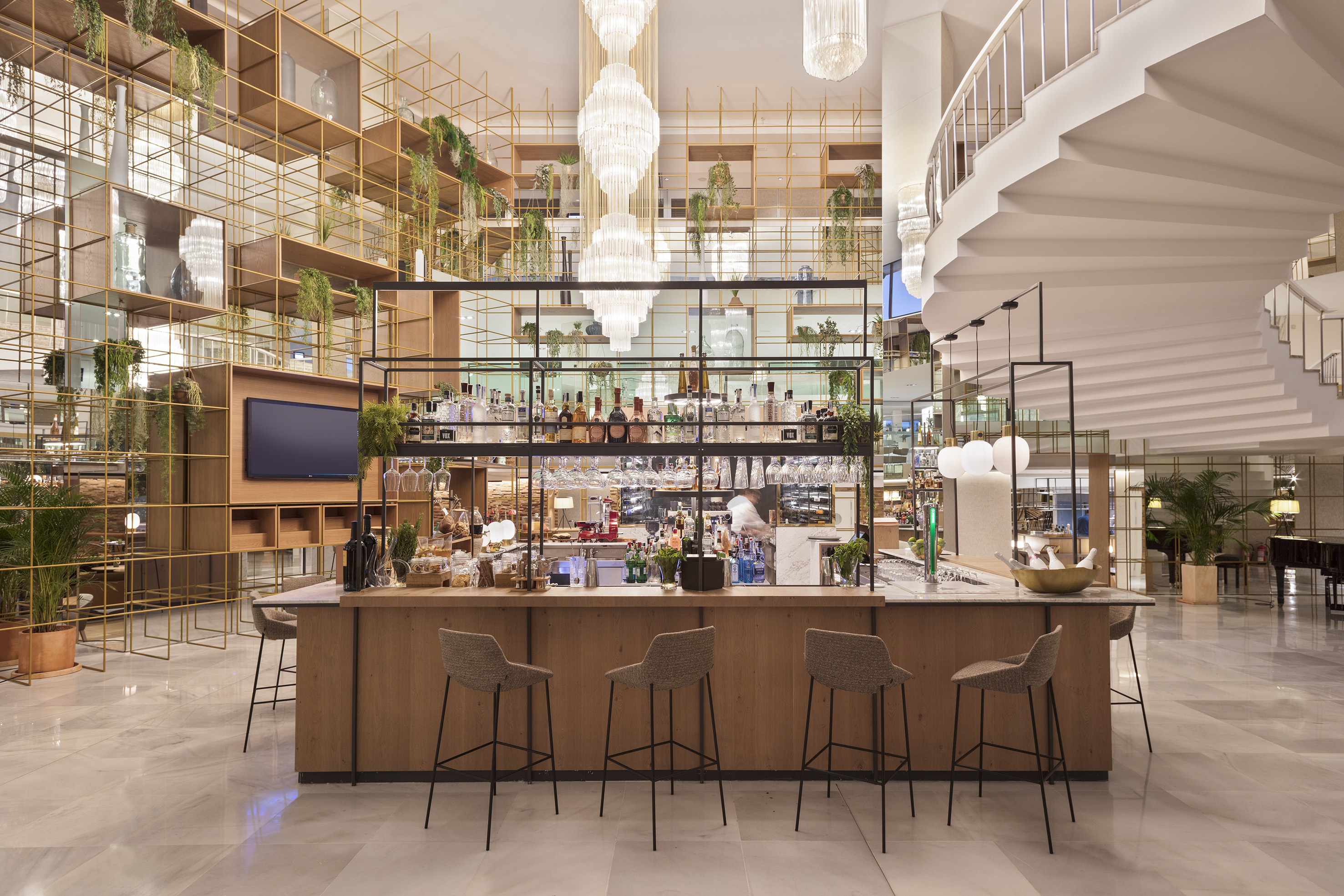 Chic hotel bar, wooden counter, golden botanical shelves, spiral staircase, chandeliers.