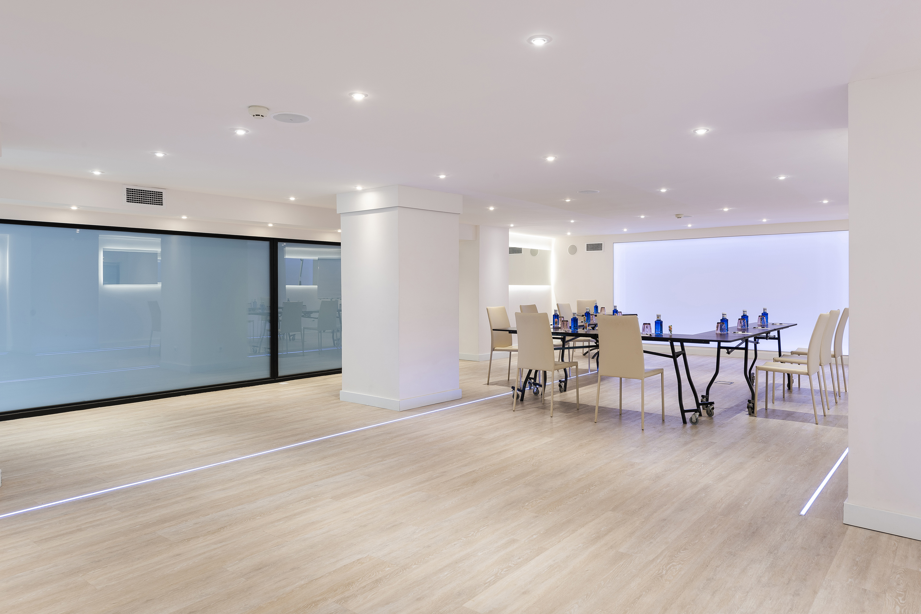Modern meeting room with wood floor, long table, chairs, and glass wall.