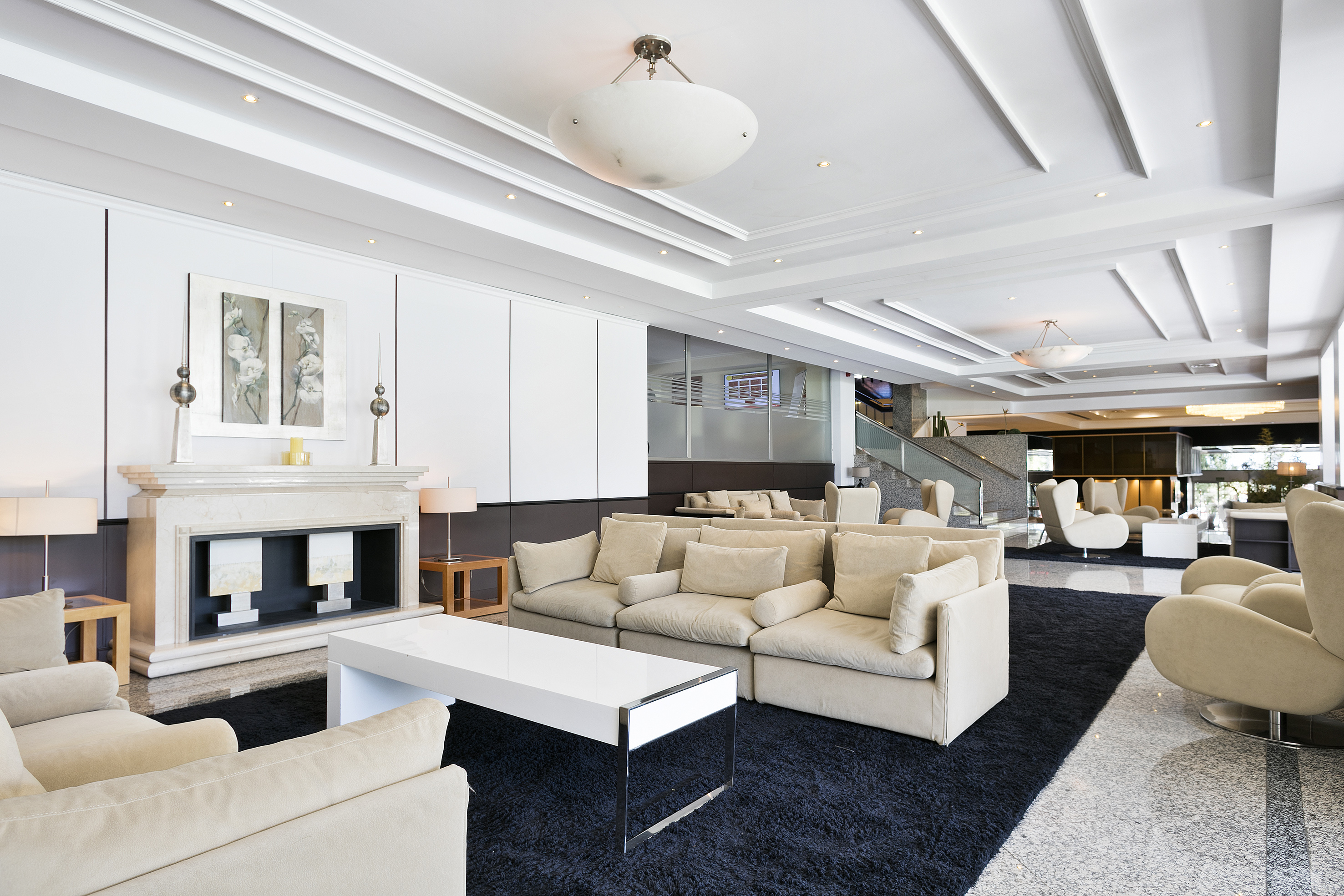 Modern hotel lounge with cream seating, black rug, and fireplace.