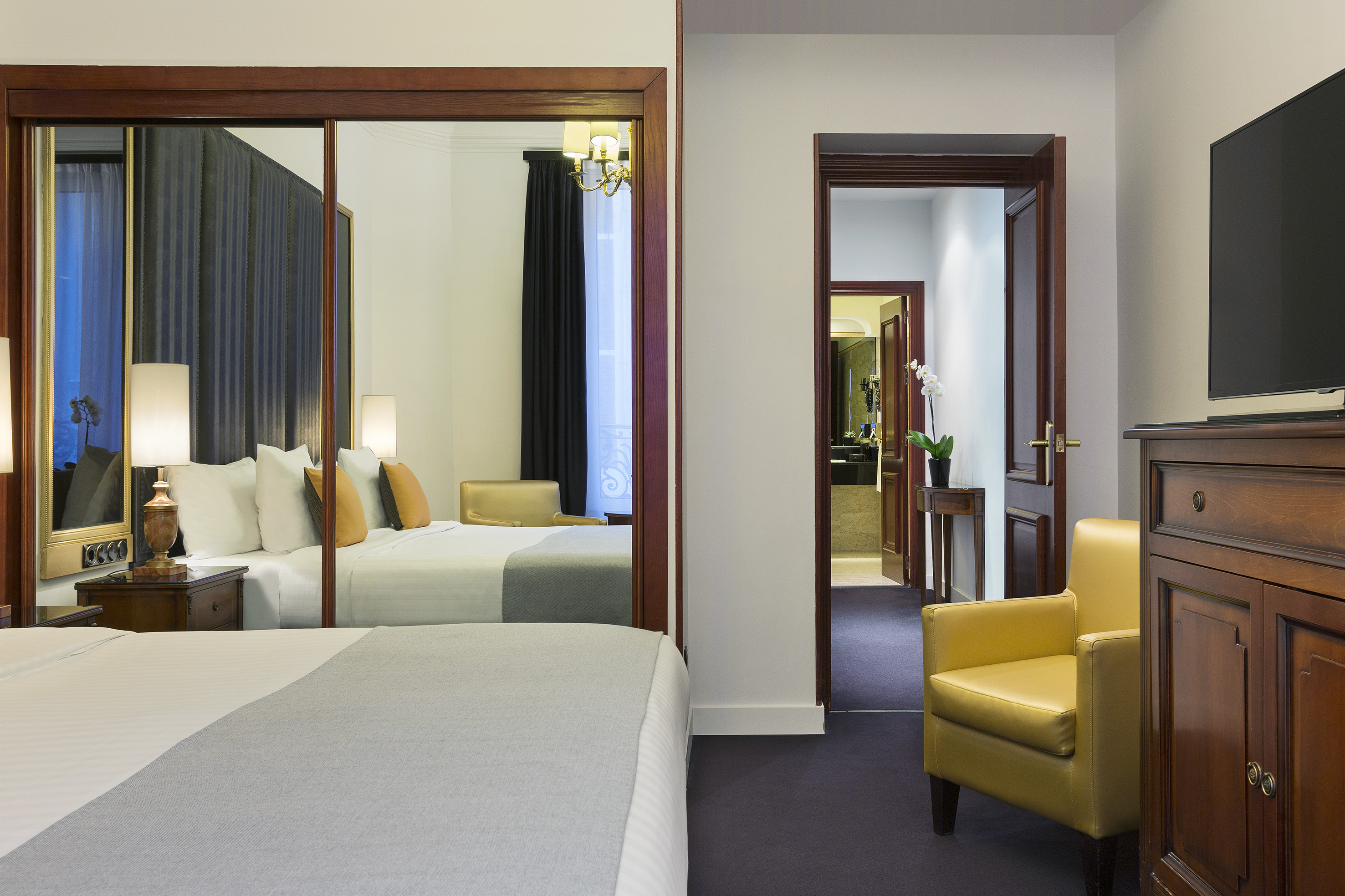 Hotel bedroom with bed, mirrored closet, yellow armchair, and bathroom.