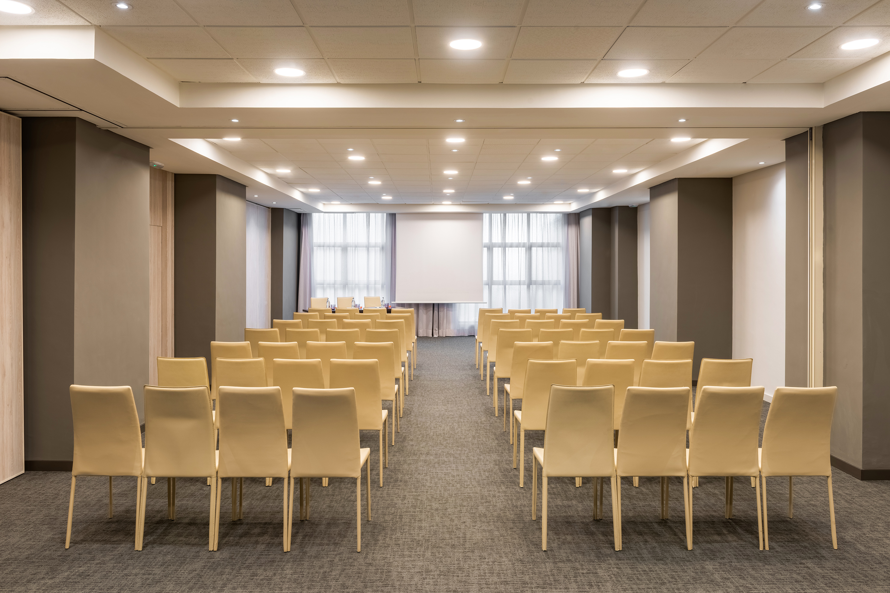 Empty modern meeting room with rows of beige chairs and a projection screen.