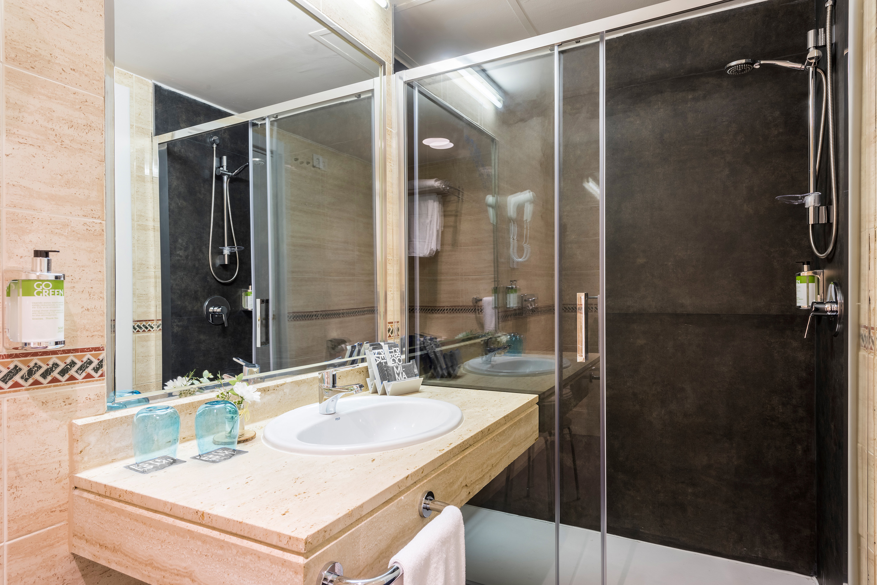 Modern hotel bathroom with stone vanity, white sink, and glass shower.
