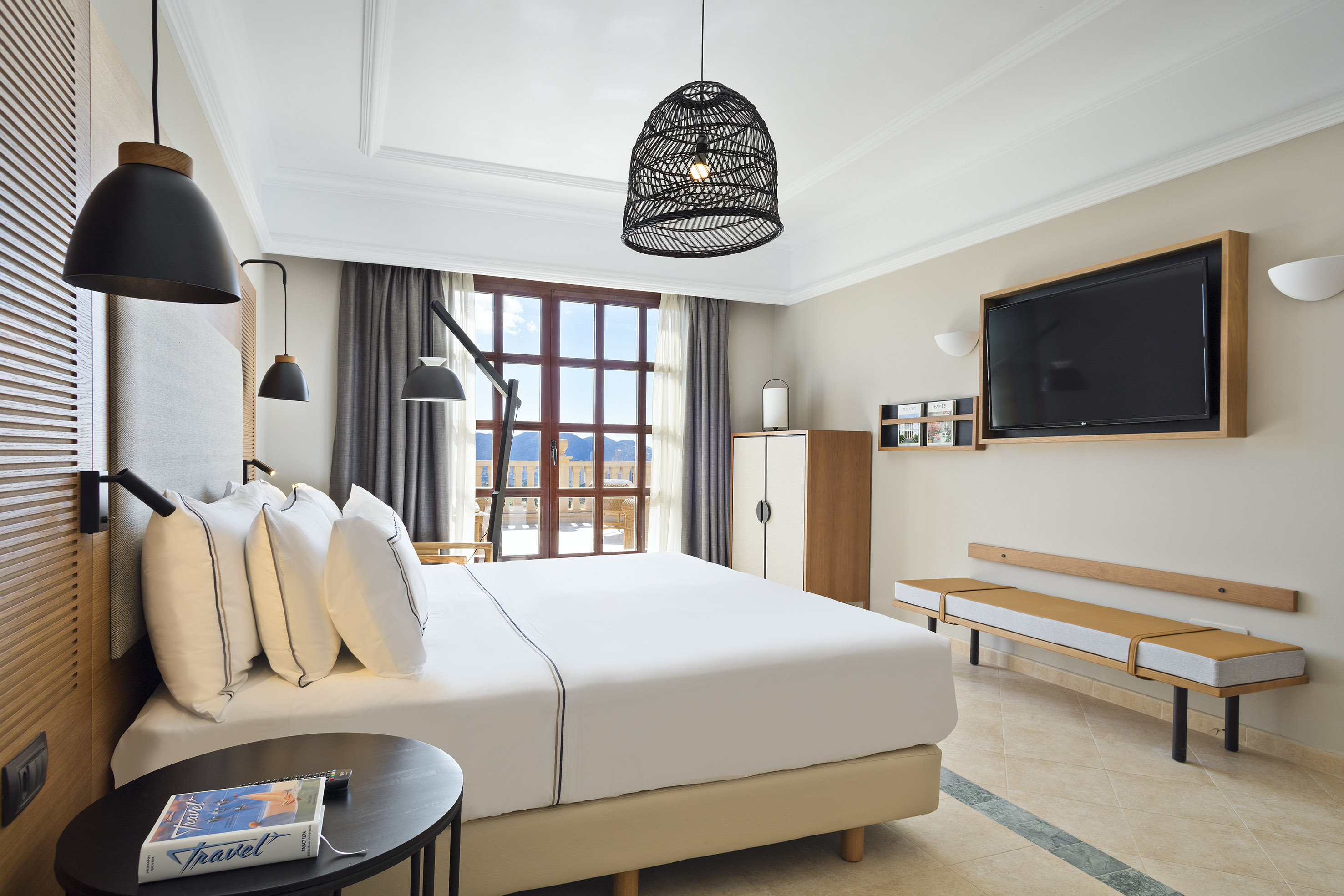 Modern hotel bedroom with king bed, stylish decor, TV, and mountain view balcony.