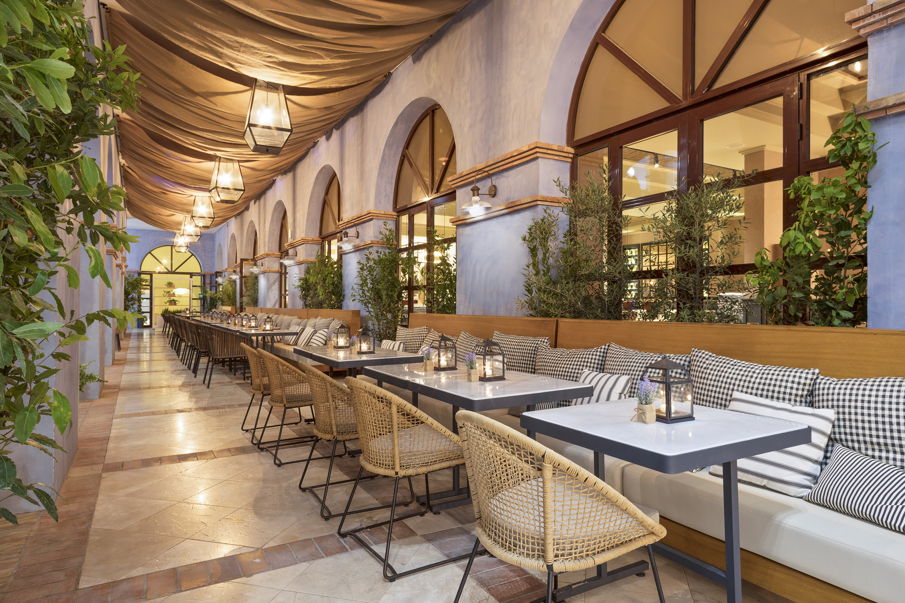 Elegant outdoor restaurant patio with woven chairs, bench seating, and ambient lighting.