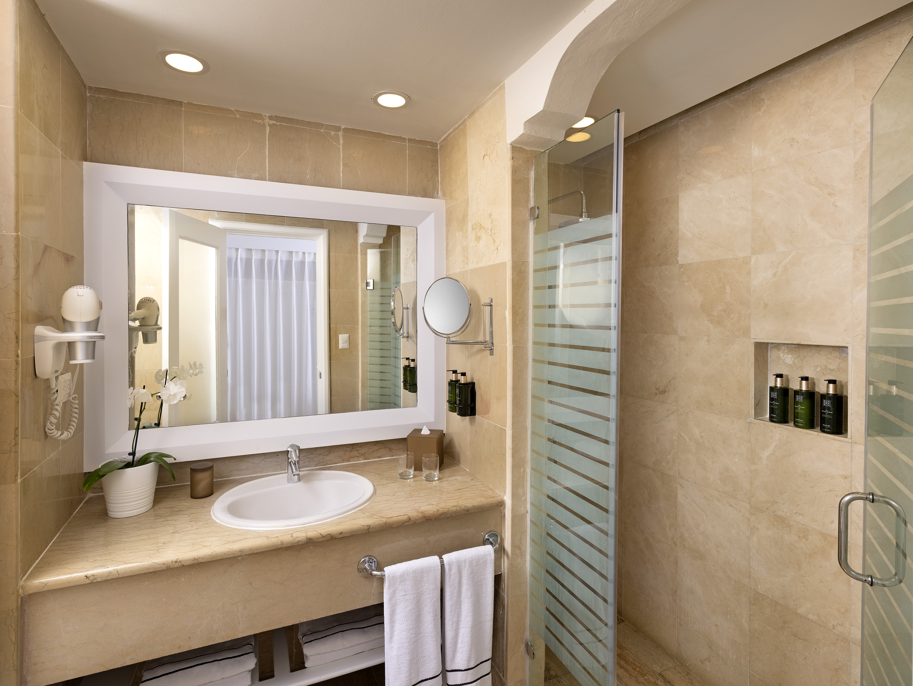 Luxury hotel bathroom with marble vanity, large mirror, and glass shower.