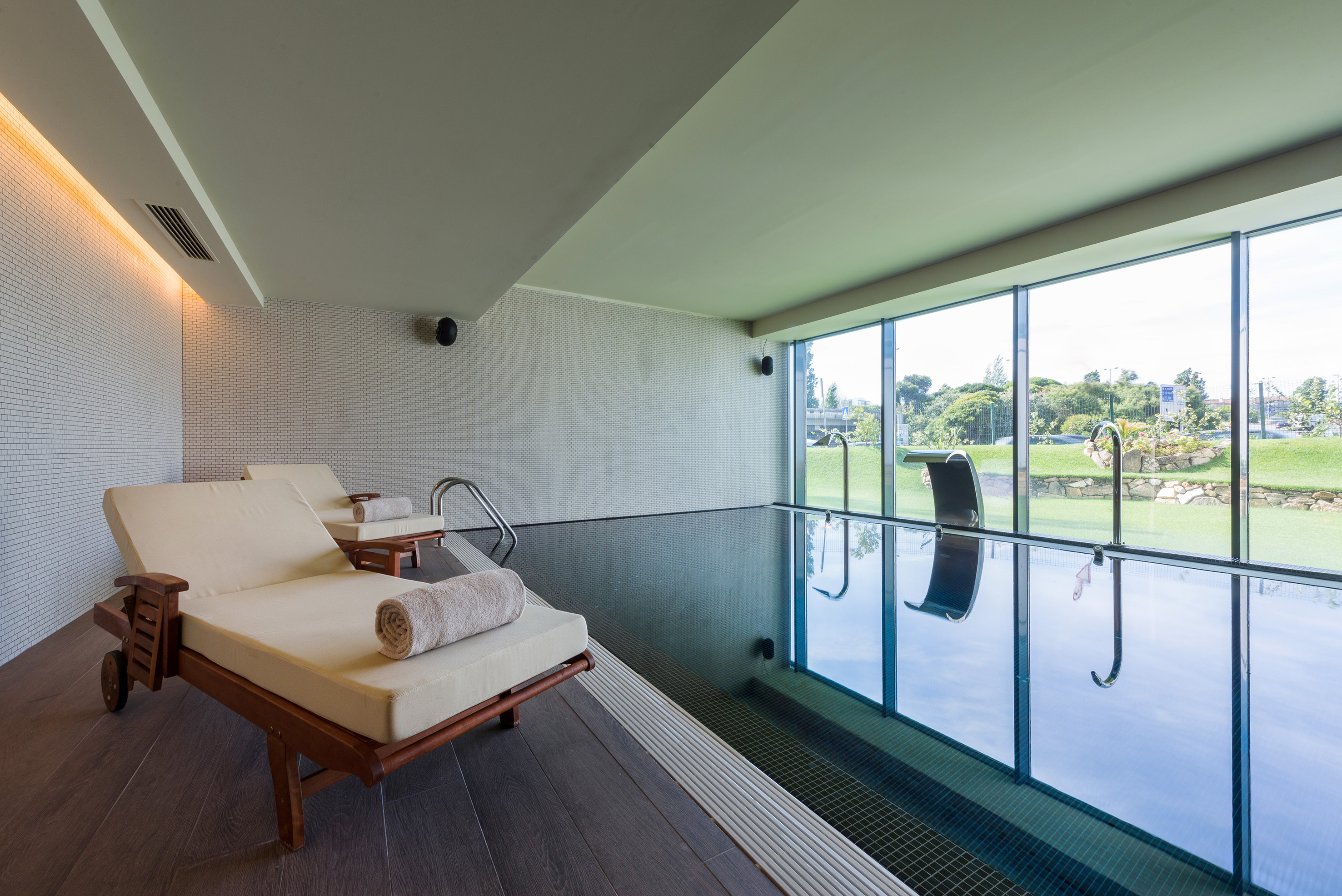 Modern indoor swimming pool with lounge chairs and large windows overlooking a garden.