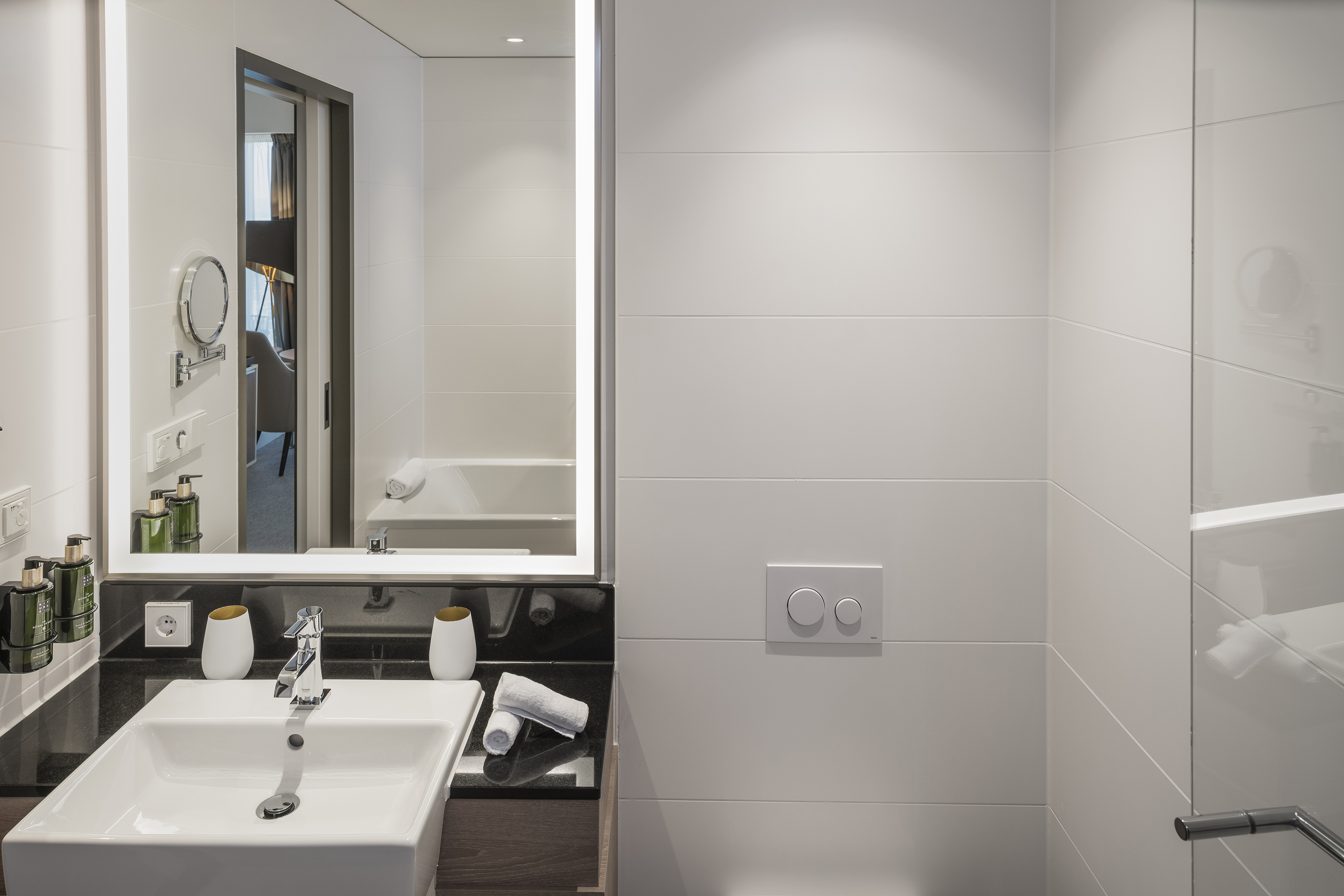Modern hotel bathroom with illuminated mirror, white sink, and tiled walls.
