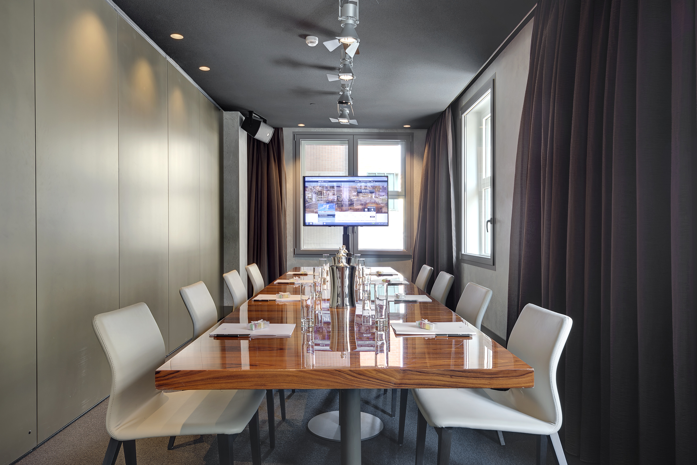 Modern meeting room with large wooden table, white chairs, and TV.