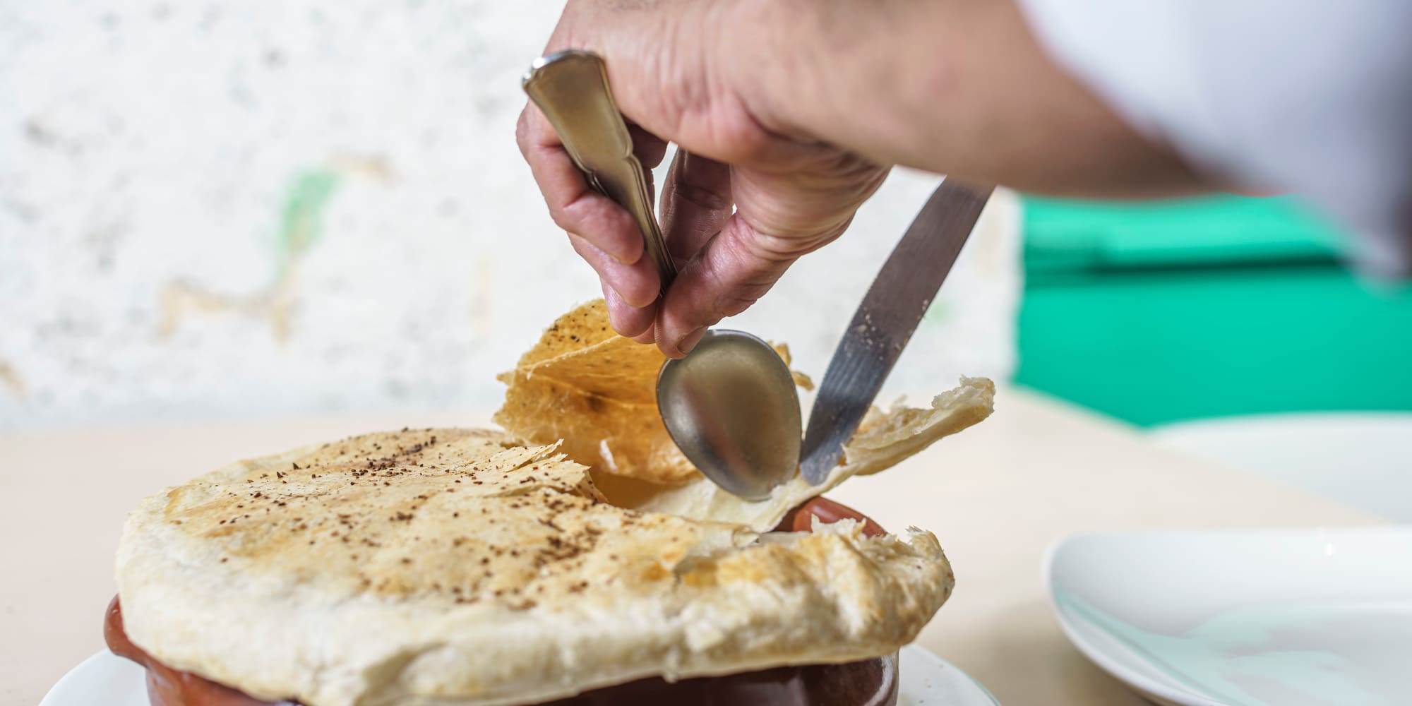 a person holding a spoon and knife over a pot pie