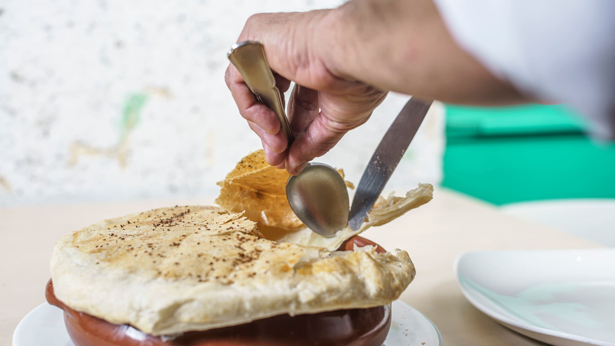 a person holding a spoon and knife over a pot pie