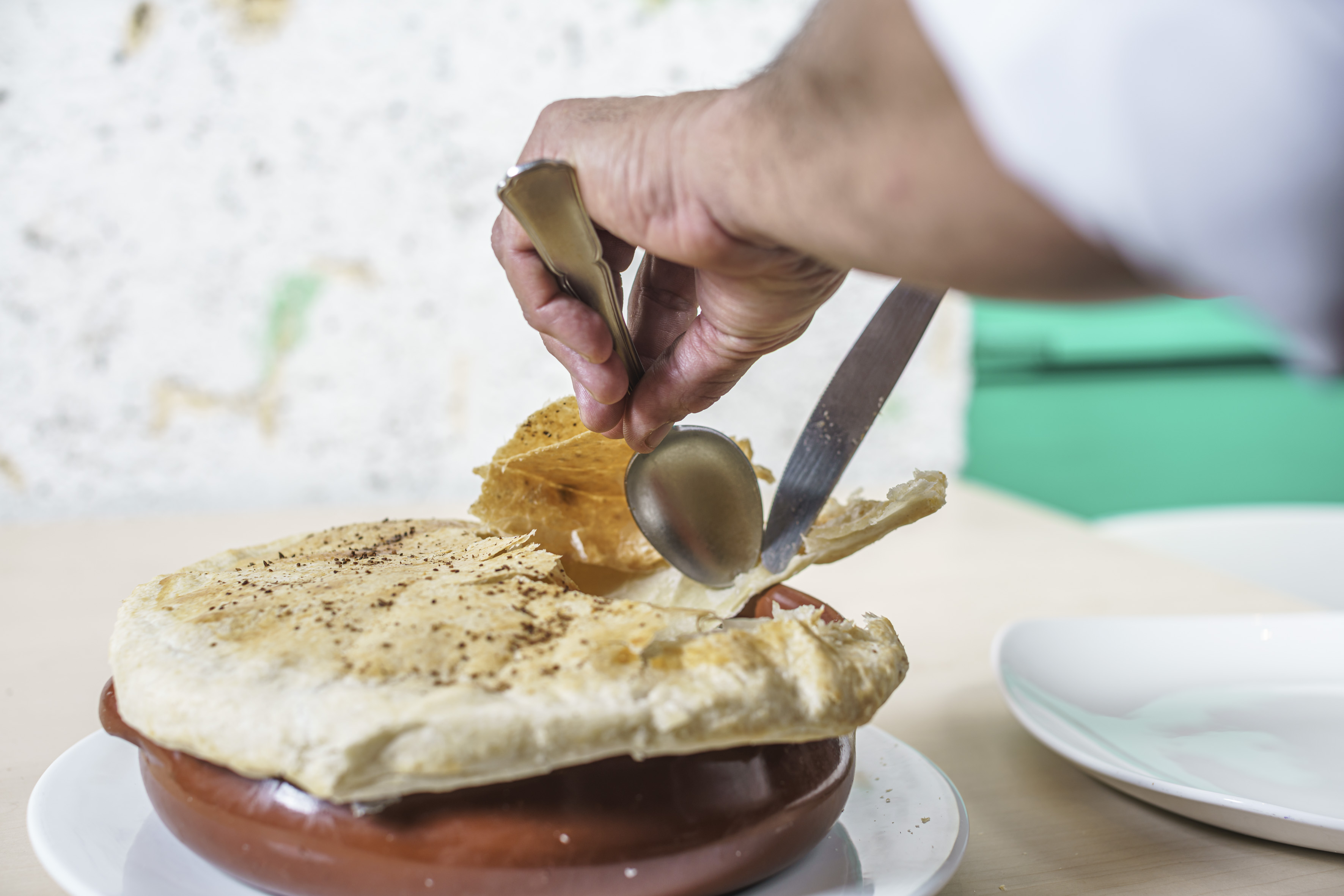 a person holding a spoon and knife over a pot pie