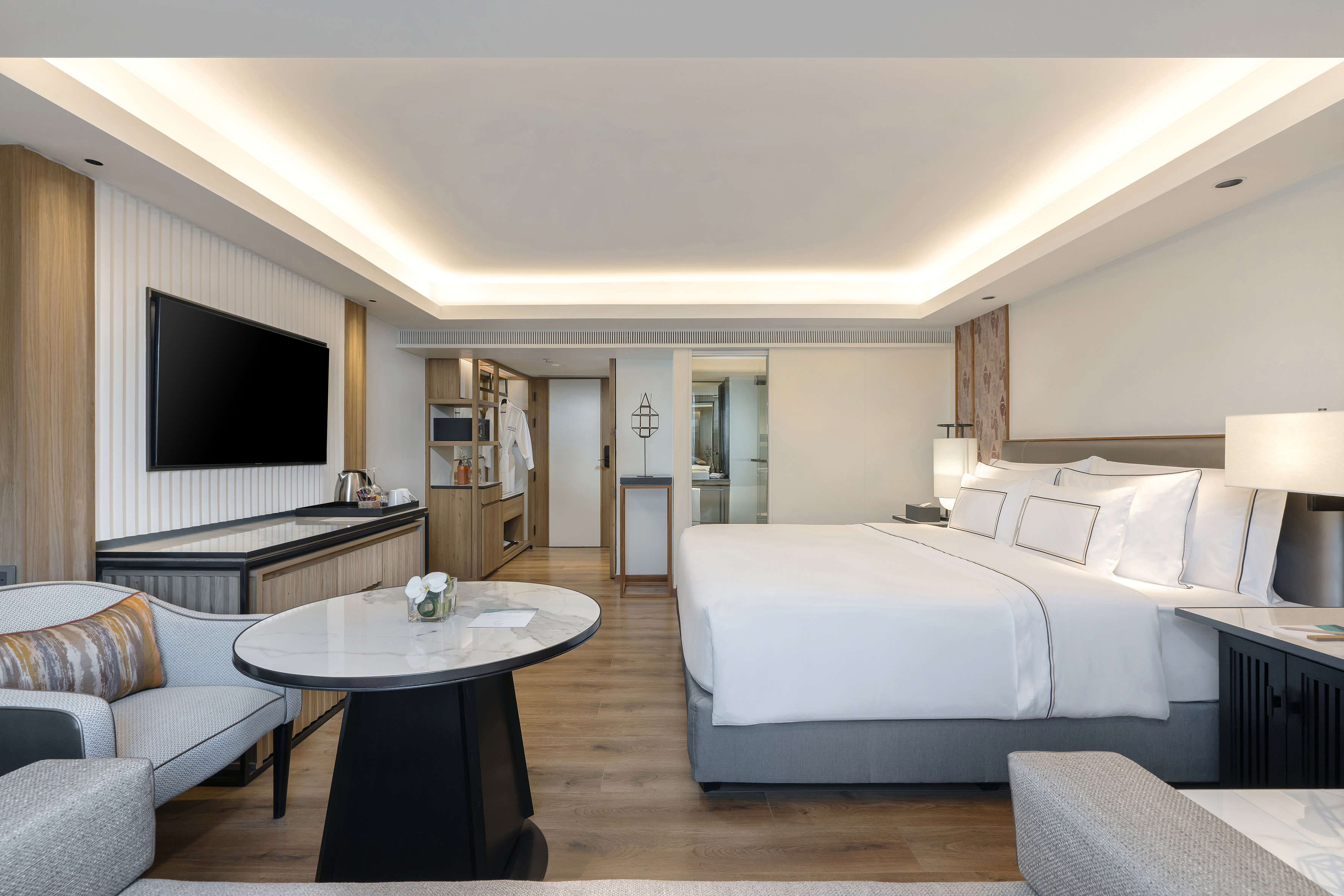 Modern hotel room with king bed, TV, seating, and elegant wood accents.