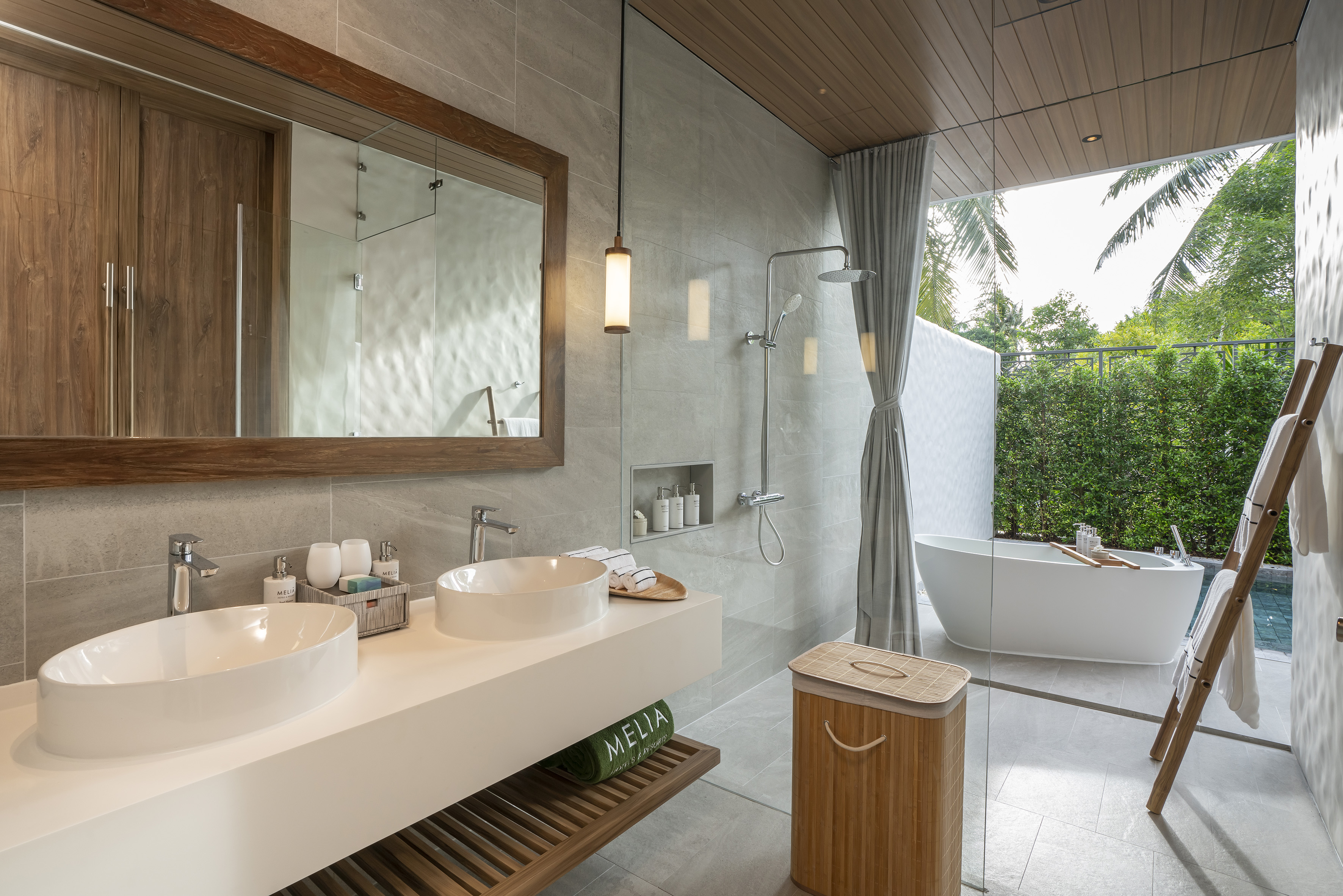 Spacious modern bathroom with double sinks, walk-in shower, freestanding tub, and outdoor tropical view.