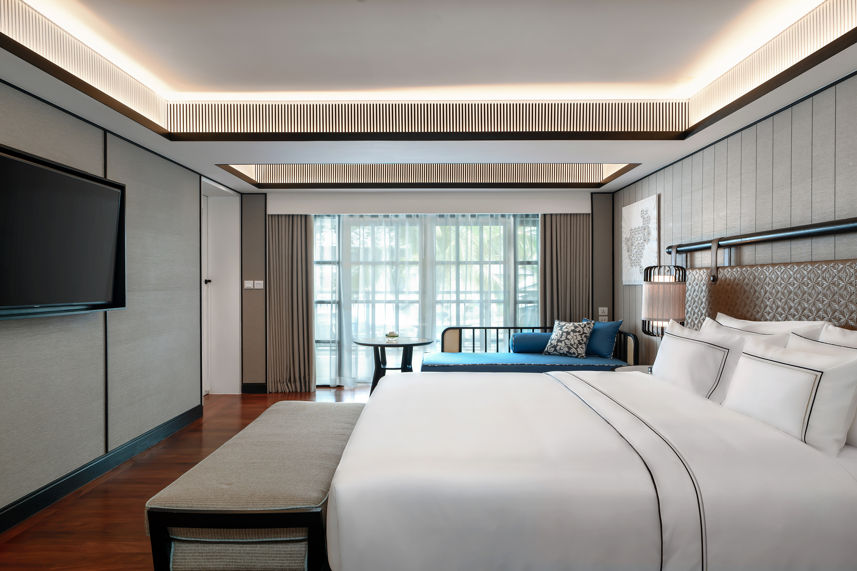 Modern luxury hotel bedroom with king bed, wall TV, and window daybed.