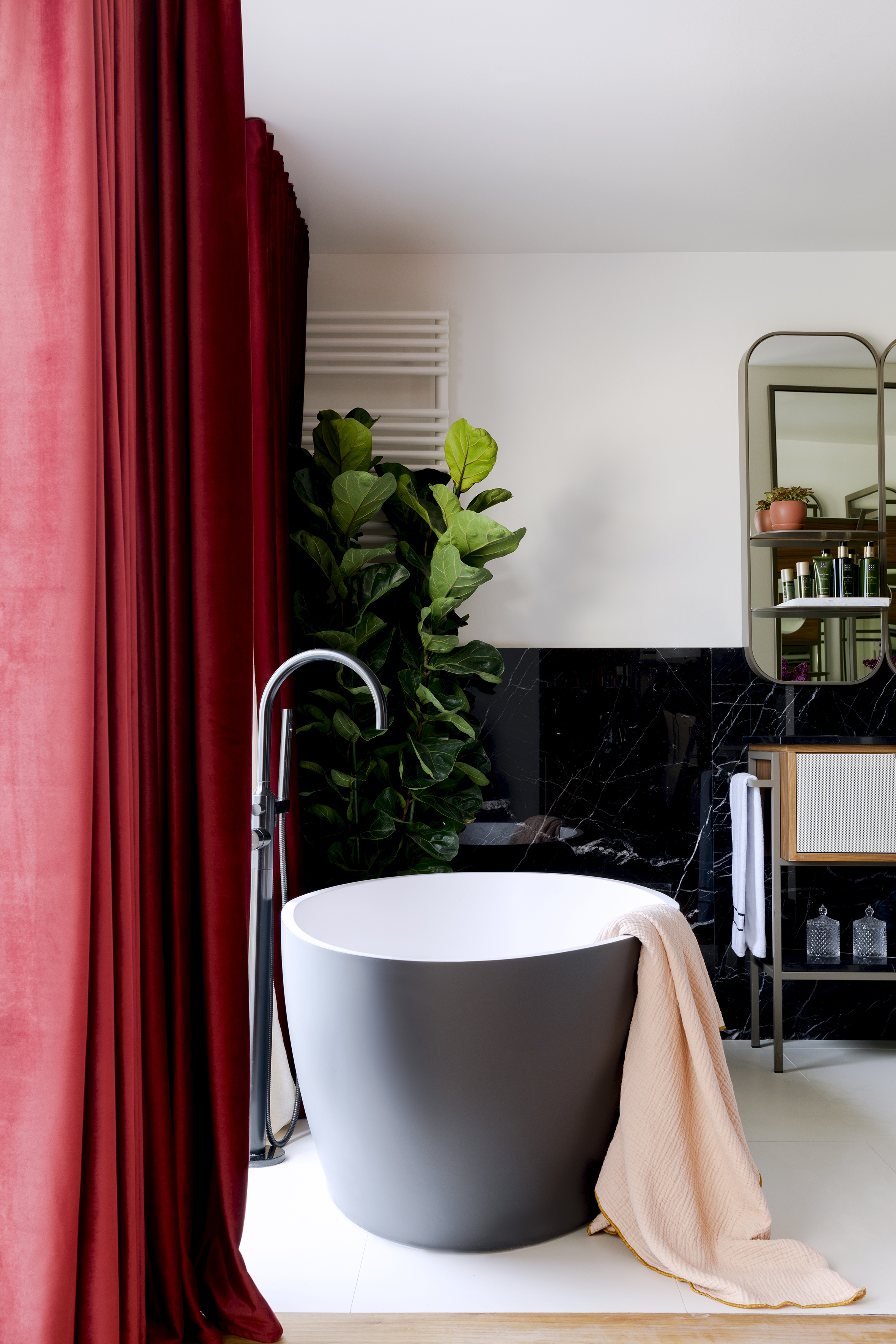 Modern bathroom with gray freestanding tub, red velvet curtains, black marble.