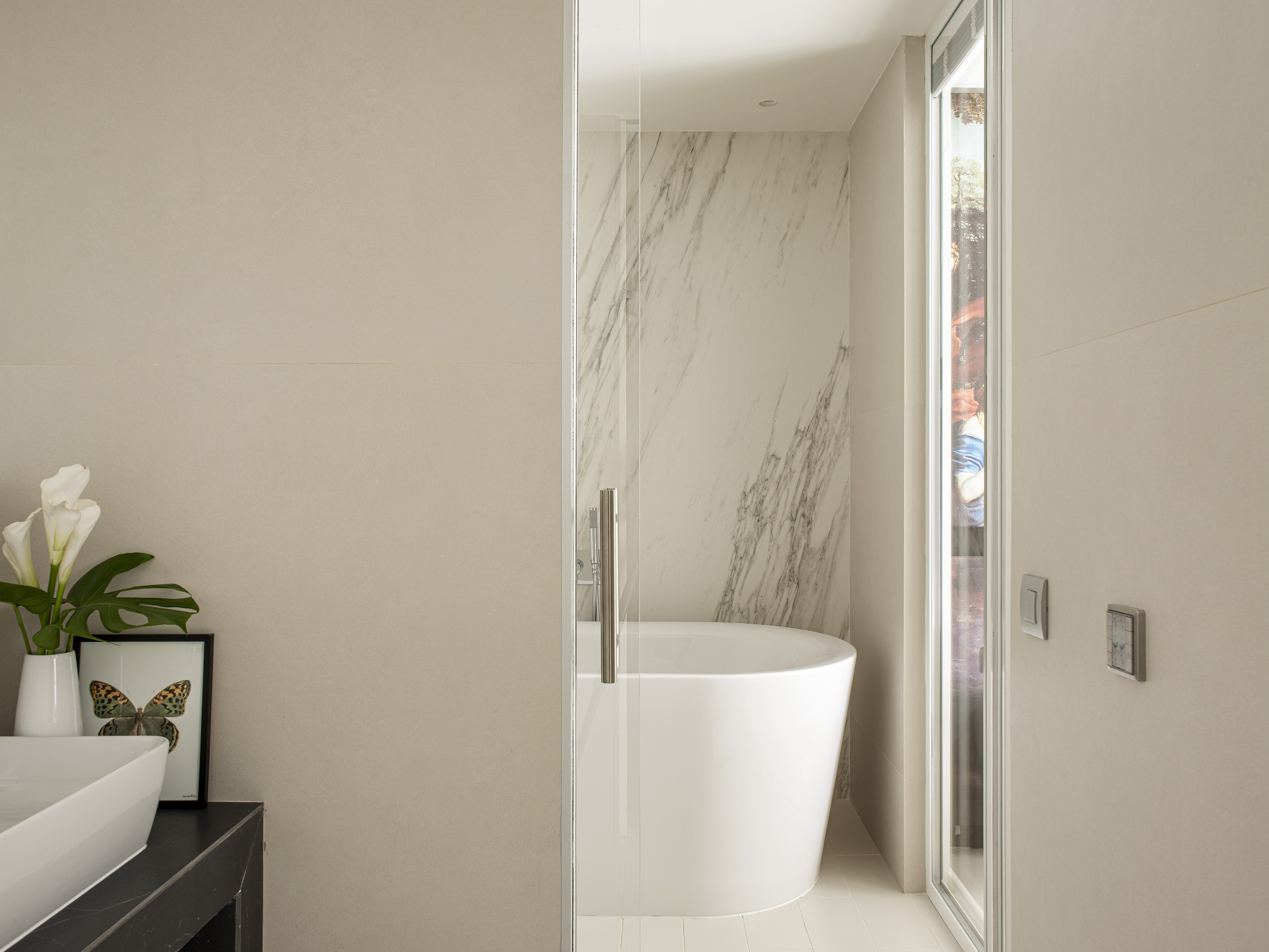 Modern bathroom: freestanding tub, marble wall, glass shower, minimalist design.