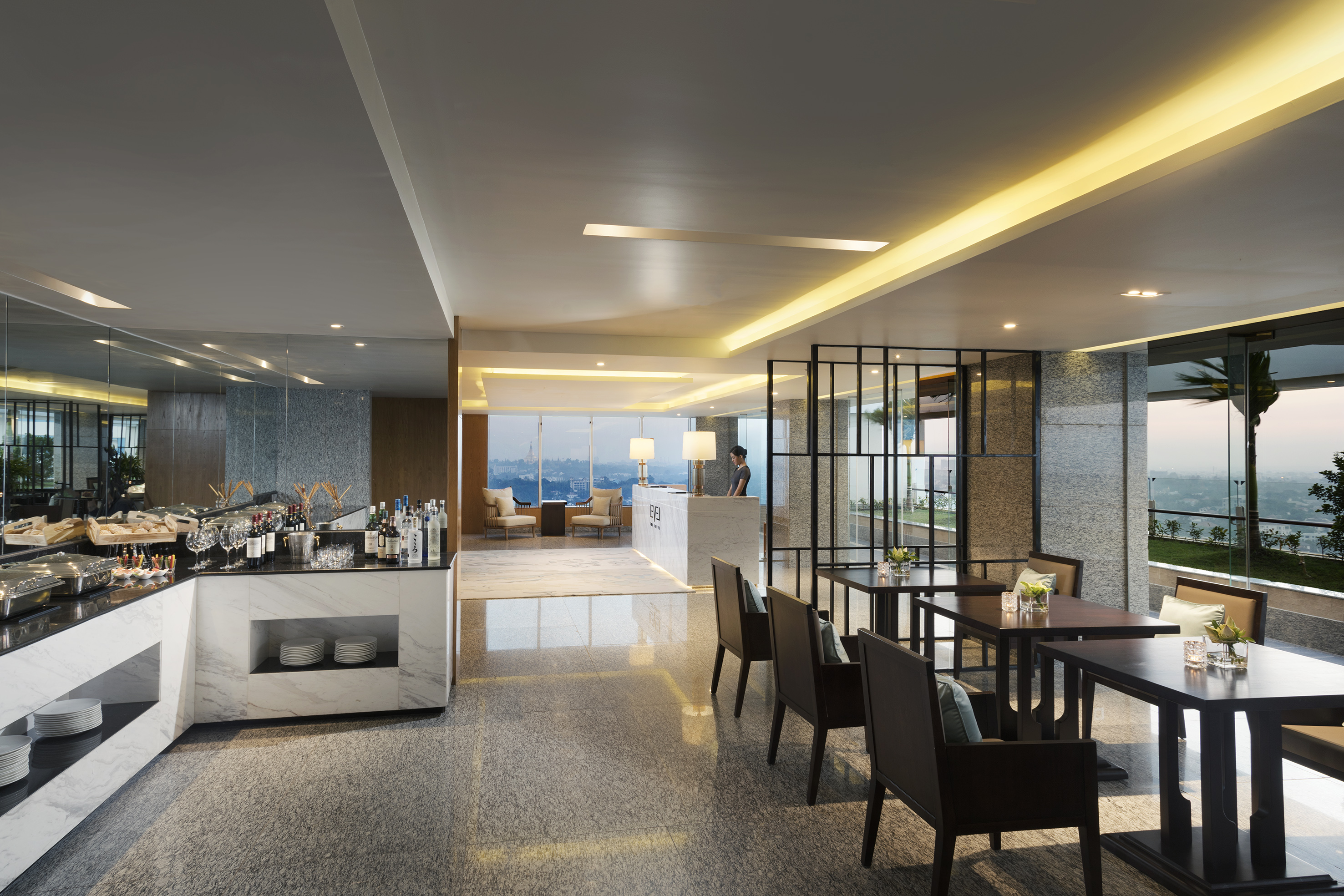 Modern hotel club lounge with buffet, bar, seating, and city view.