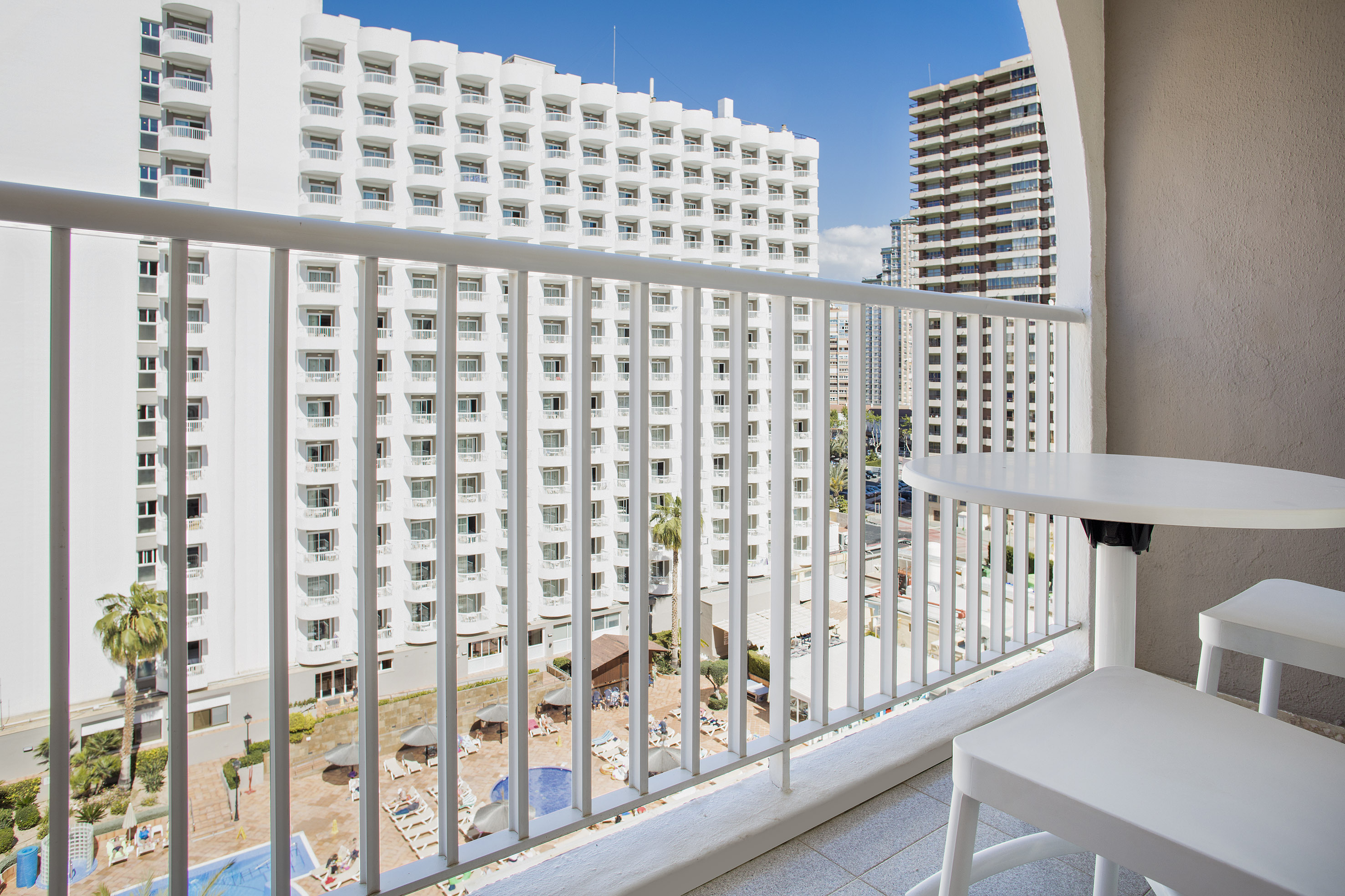 Balcony overlooking white hotel buildings, swimming pool, and city.