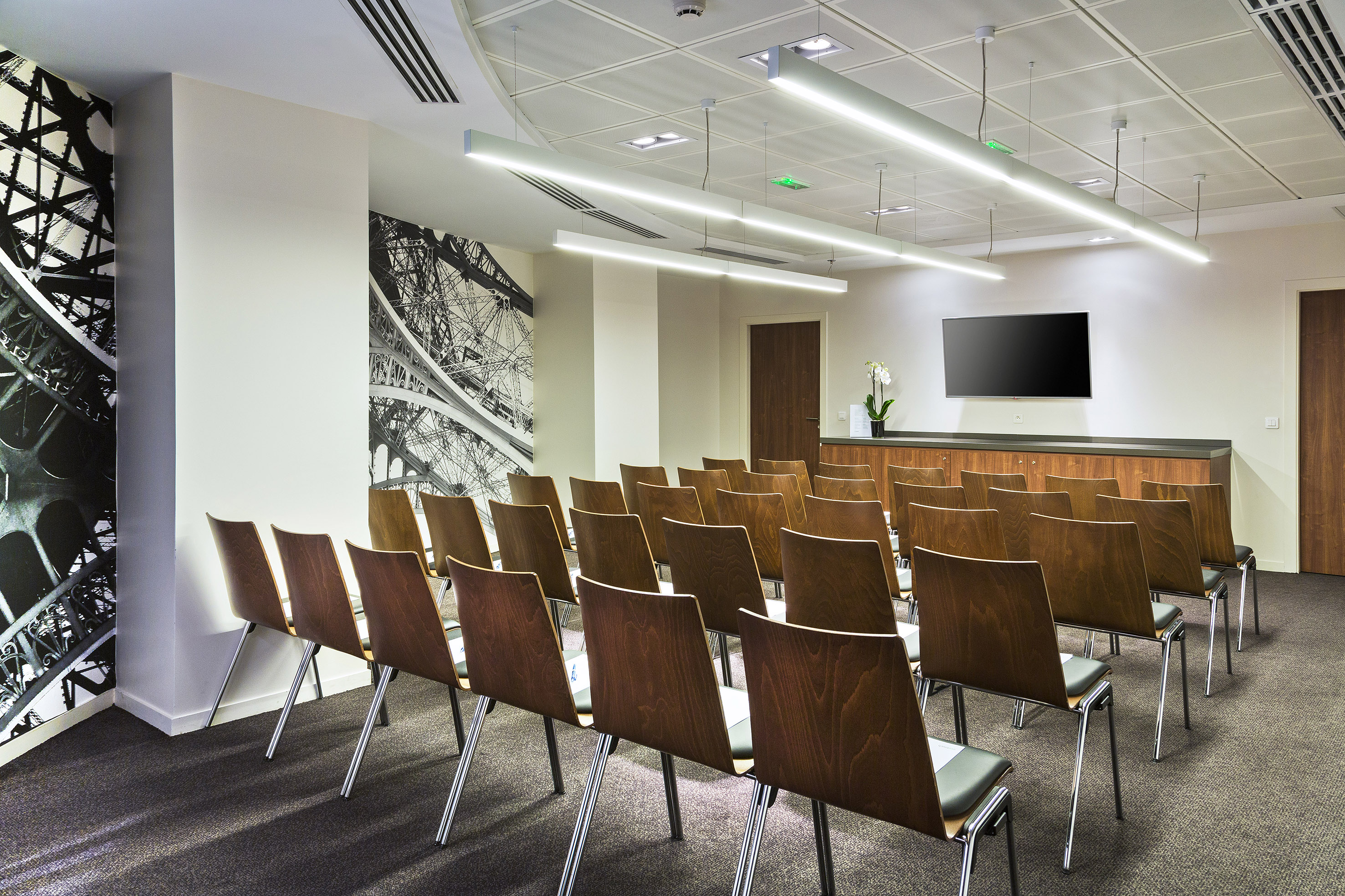 Modern conference room with rows of chairs, large TV, and Eiffel Tower wall design.