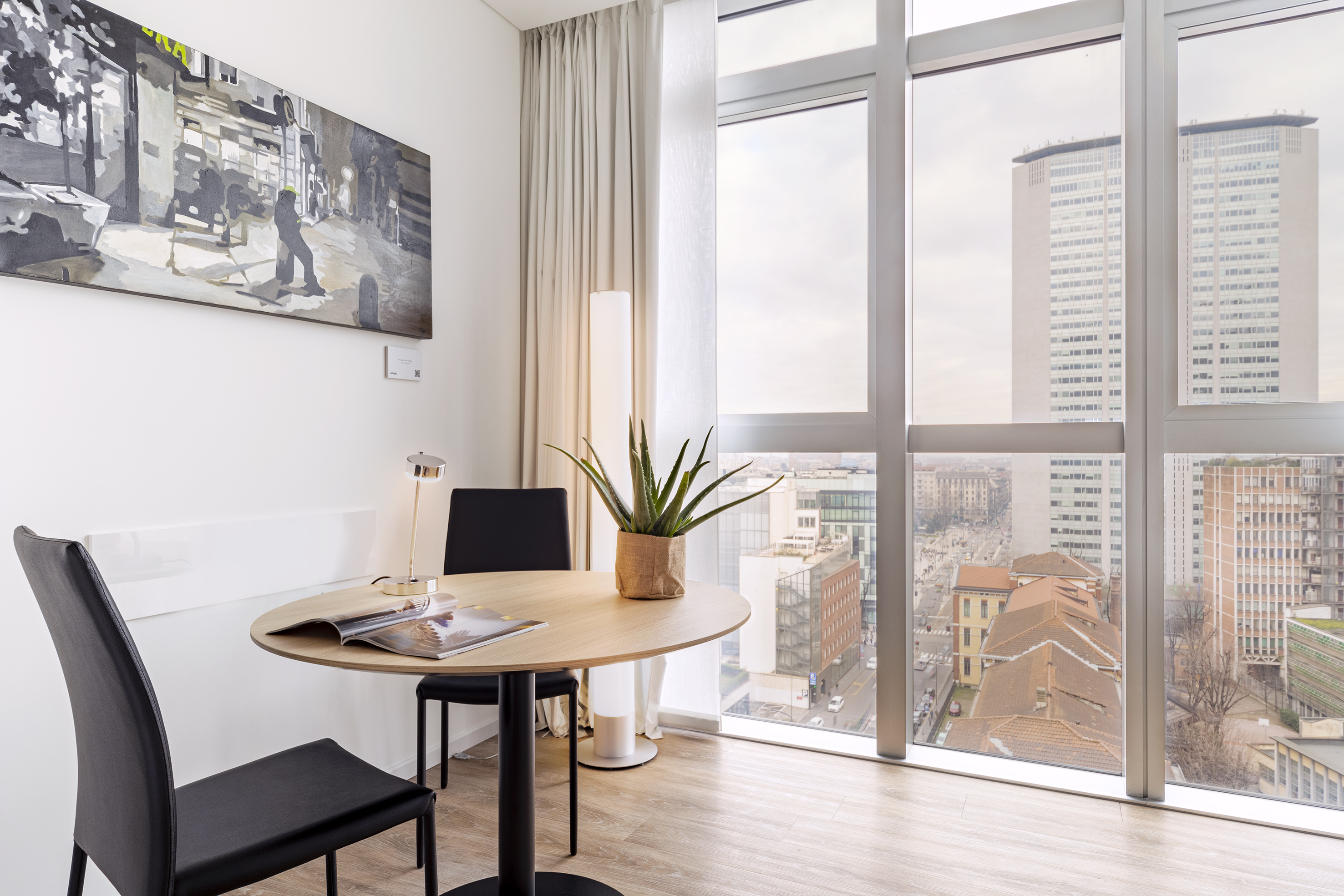 Modern hotel room with city view, round dining table, and wall art.