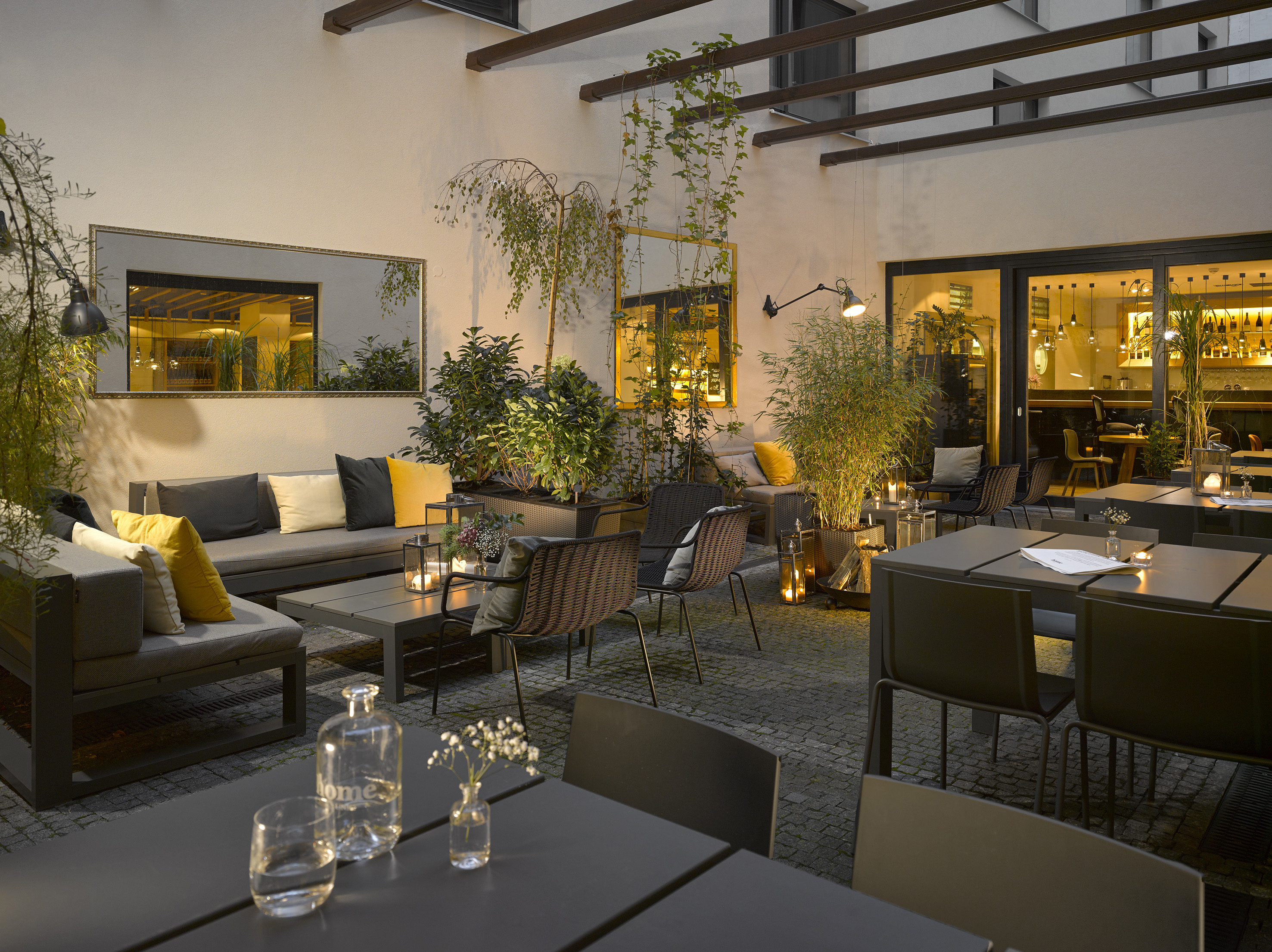 Warmly lit outdoor patio with modern lounge seating and green plants.