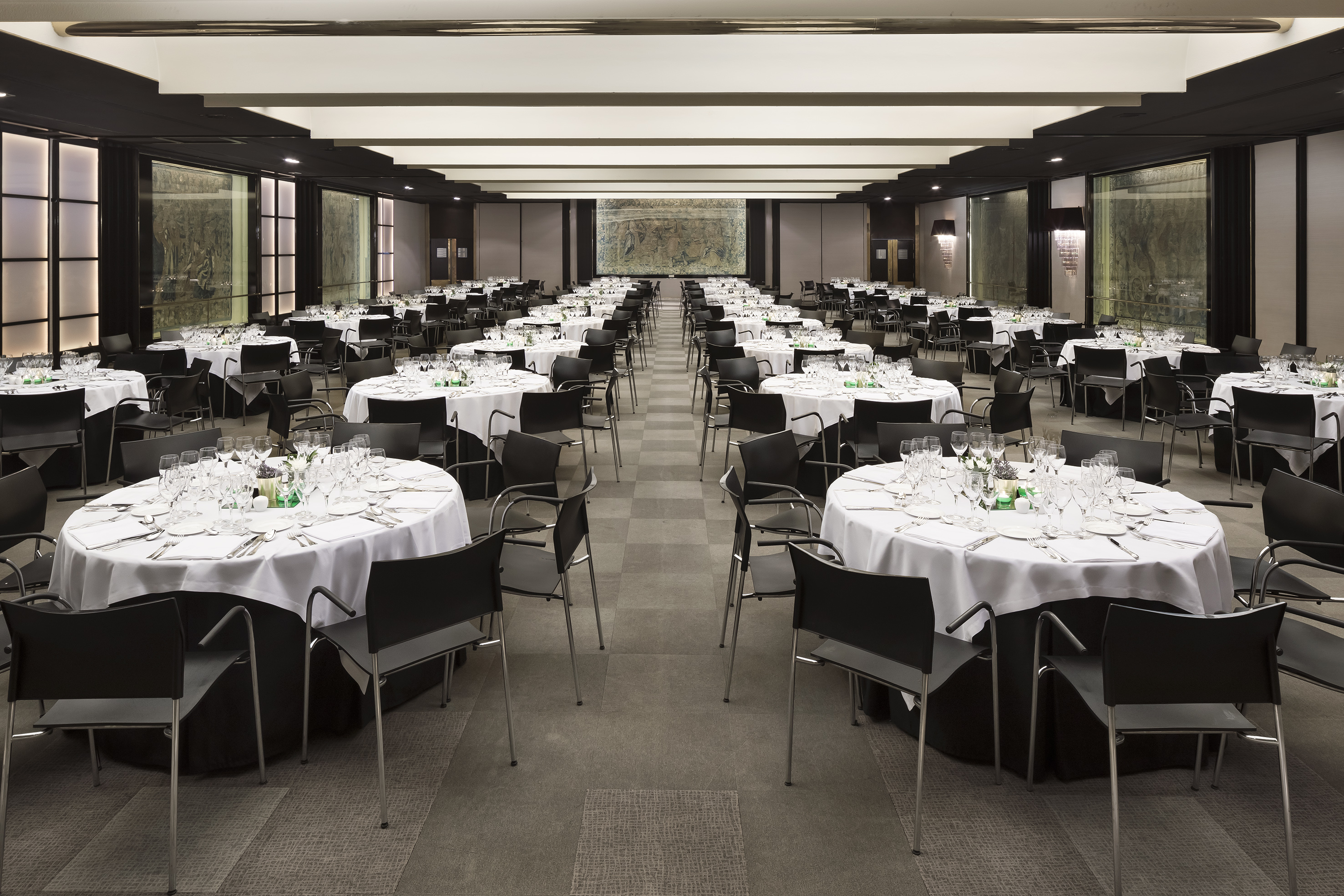 Spacious ballroom setup with round tables, white linens, black chairs for an event.